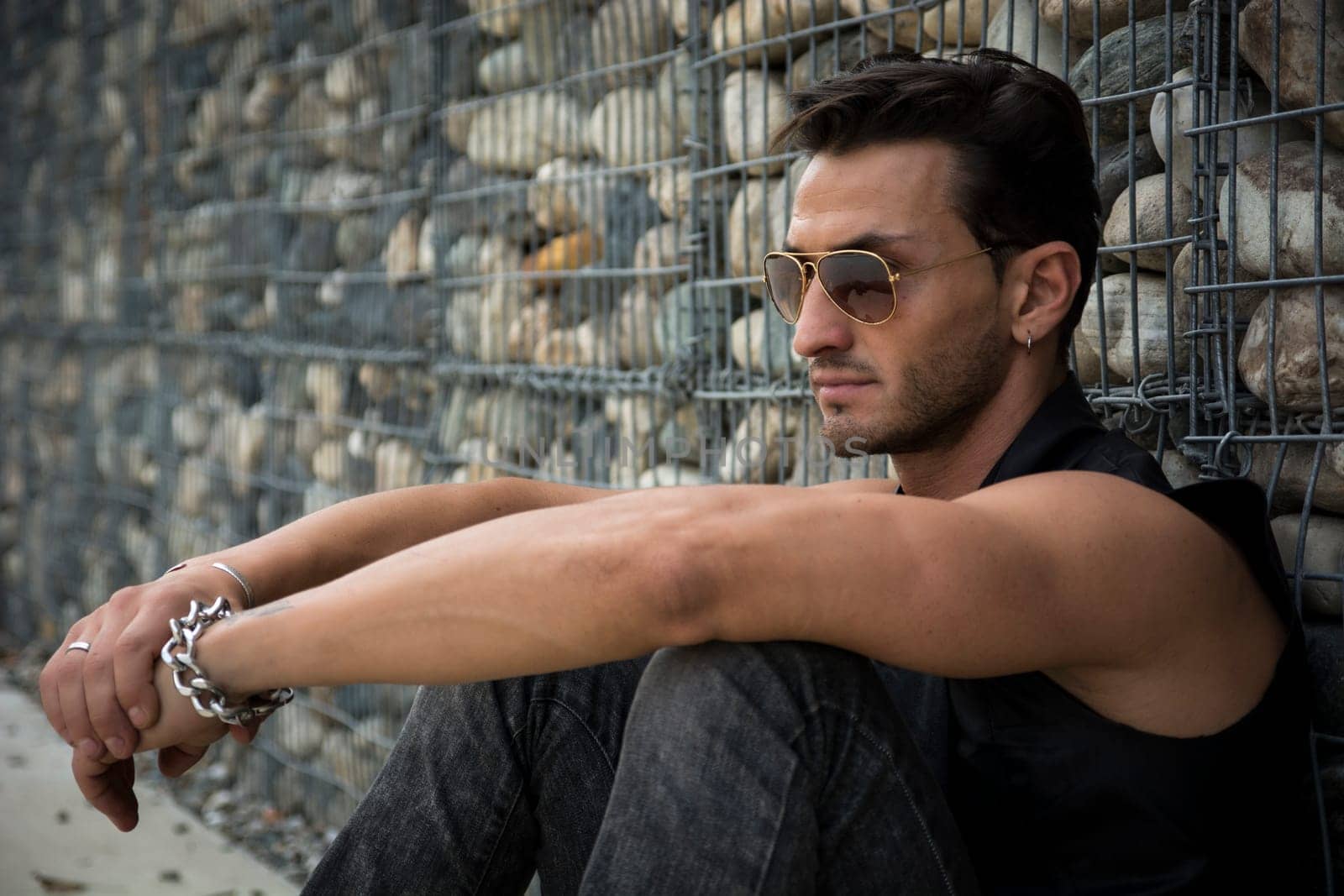 Handsome man outdoor sitting against front of stone wall  looking away