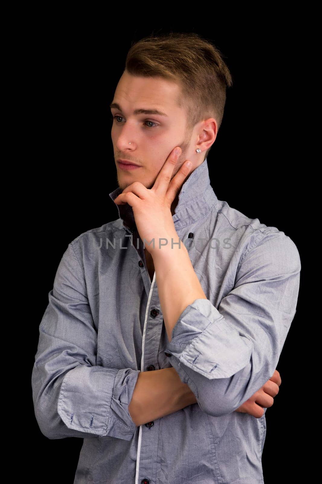 Attractive young man thinking, looking away with hand on his chin, on black background