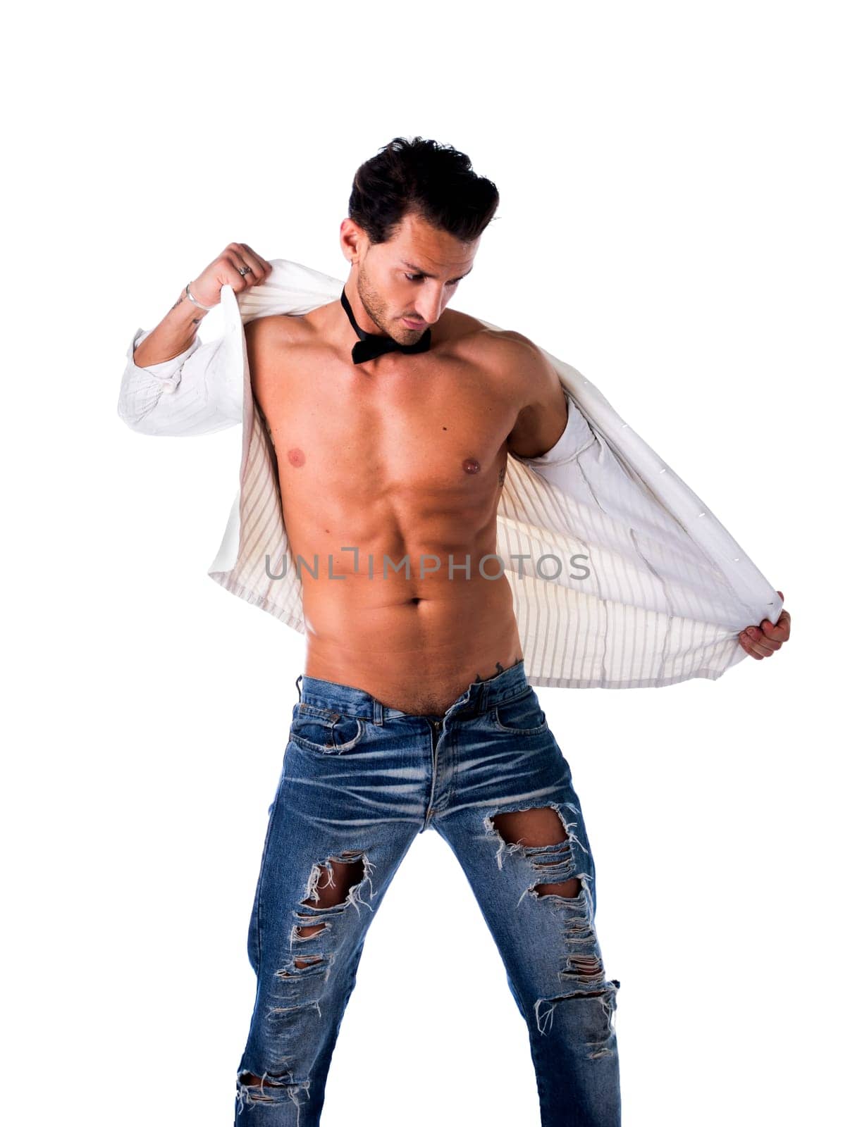 Handsome lean, man in jeans taking off shirt, looking down, isolated on white
