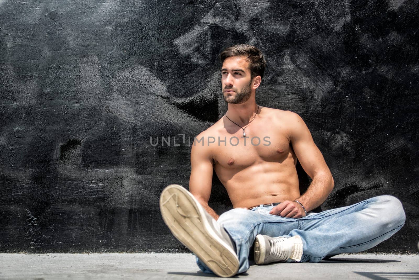 Handsome bearded shirtless young man sitting outdoors in urban environment