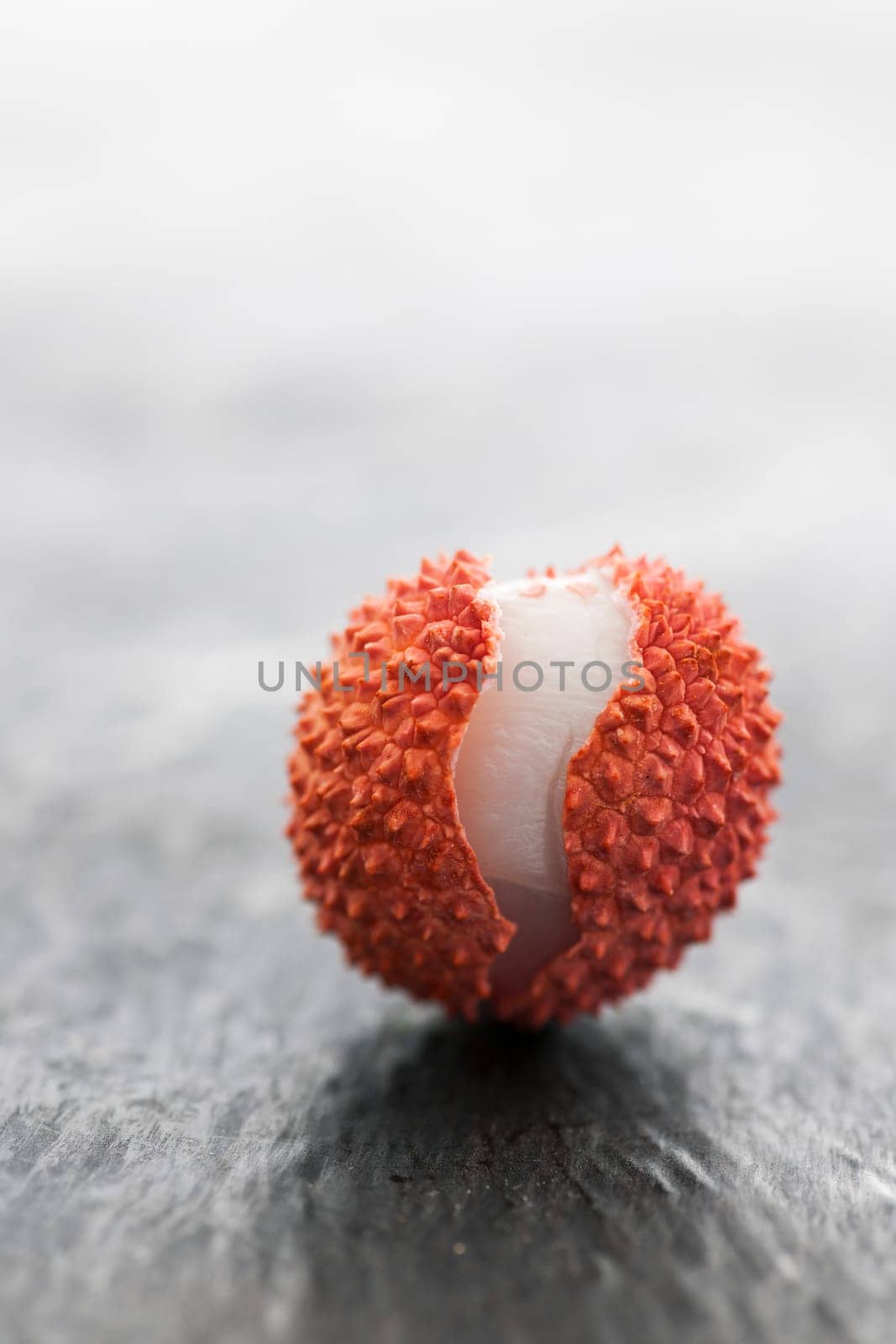 Studio shot of a lychee fruit with an open peel on slate plate.