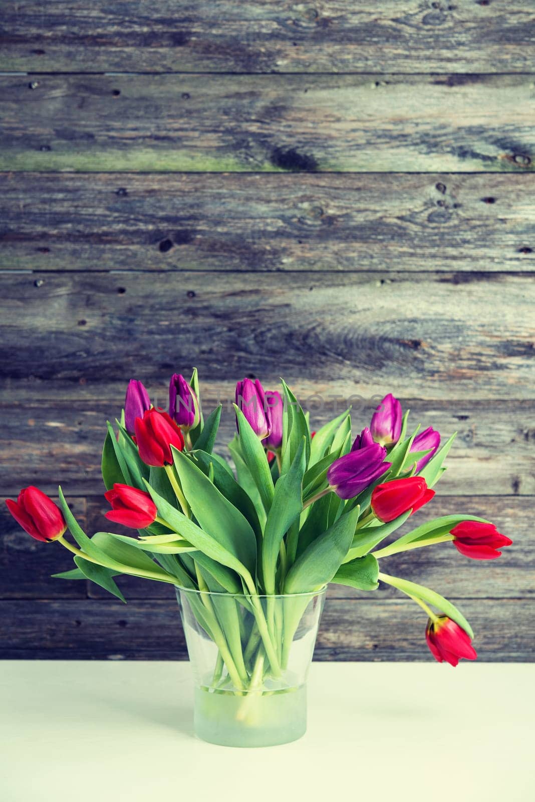 bouquet of red and violet tulips  in vase in front of wooden background