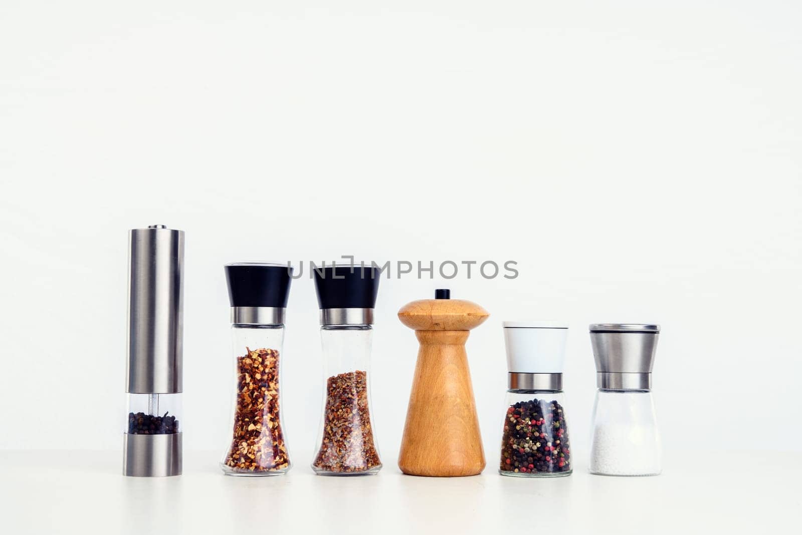 different spice mills with salt,pepper and other herbs in front of white background