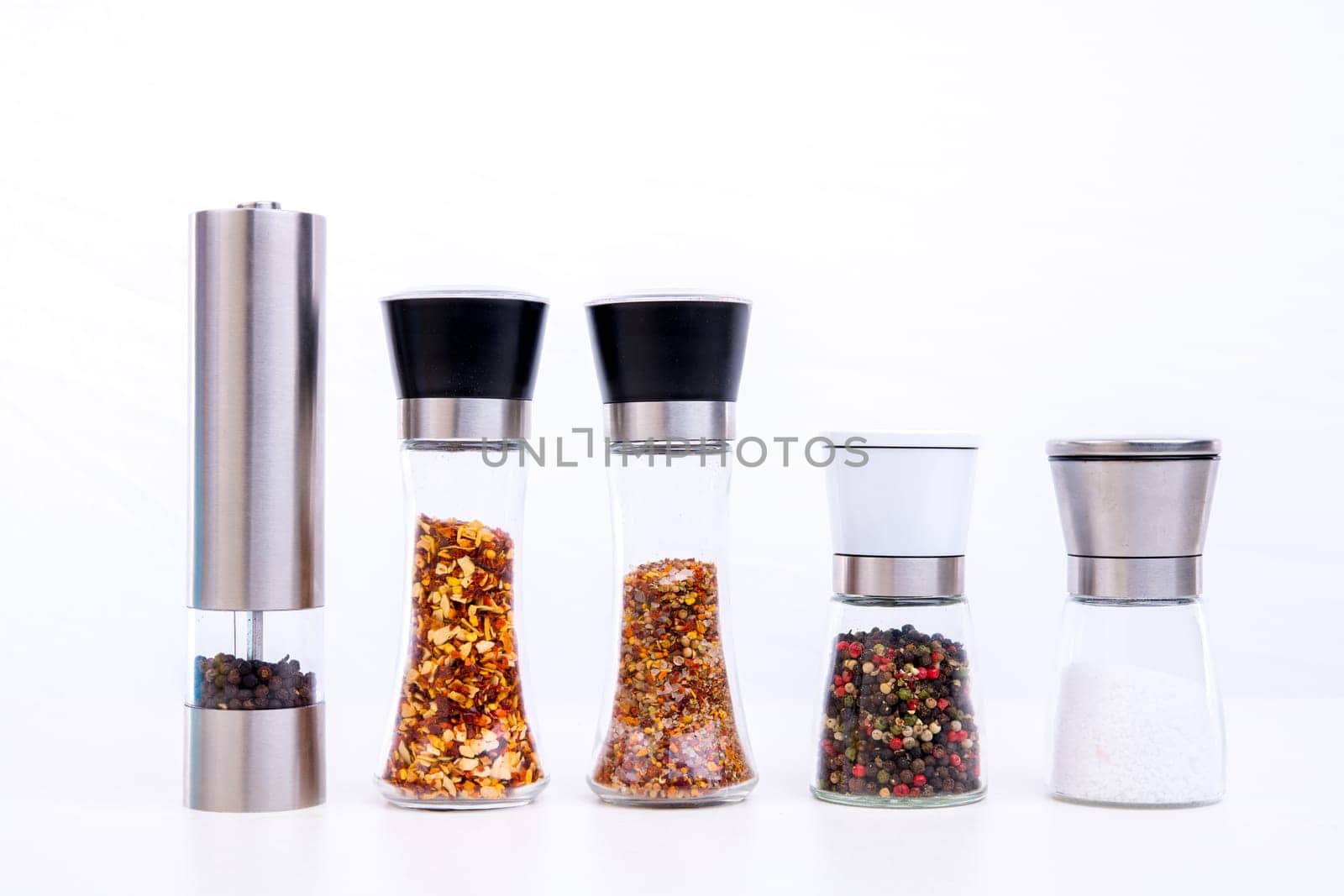 different spice mills with salt,pepper and other herbs in front of white background