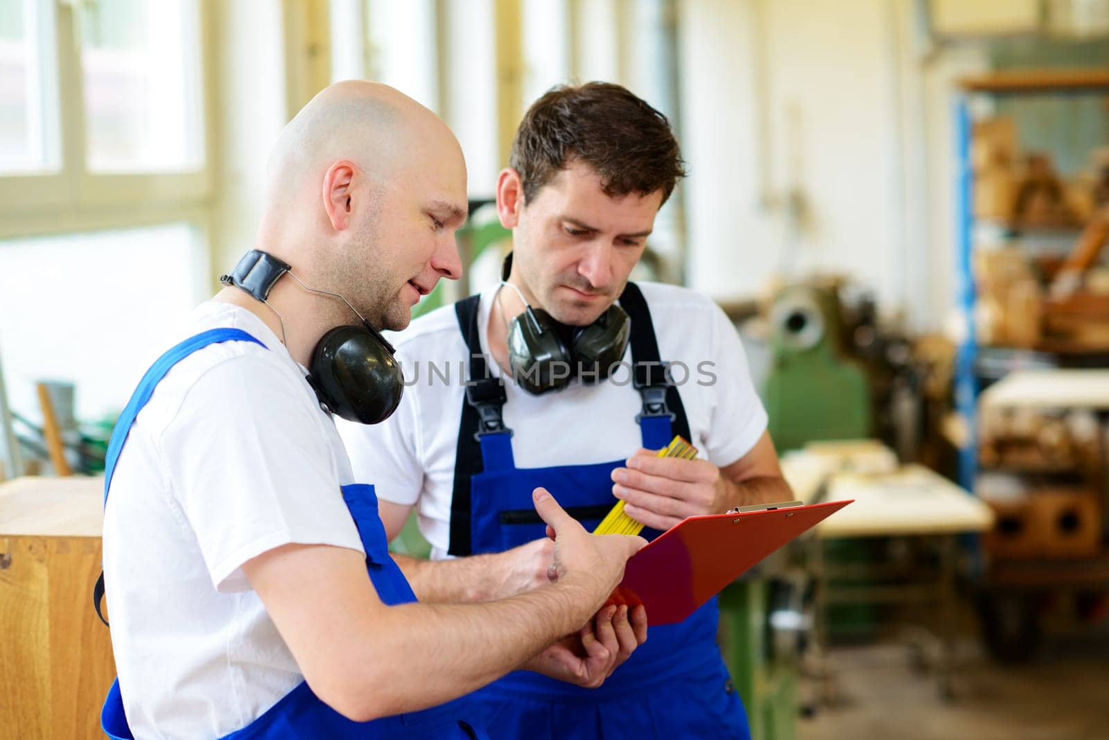 two worker in blue dungarees in a carpenter's workshop