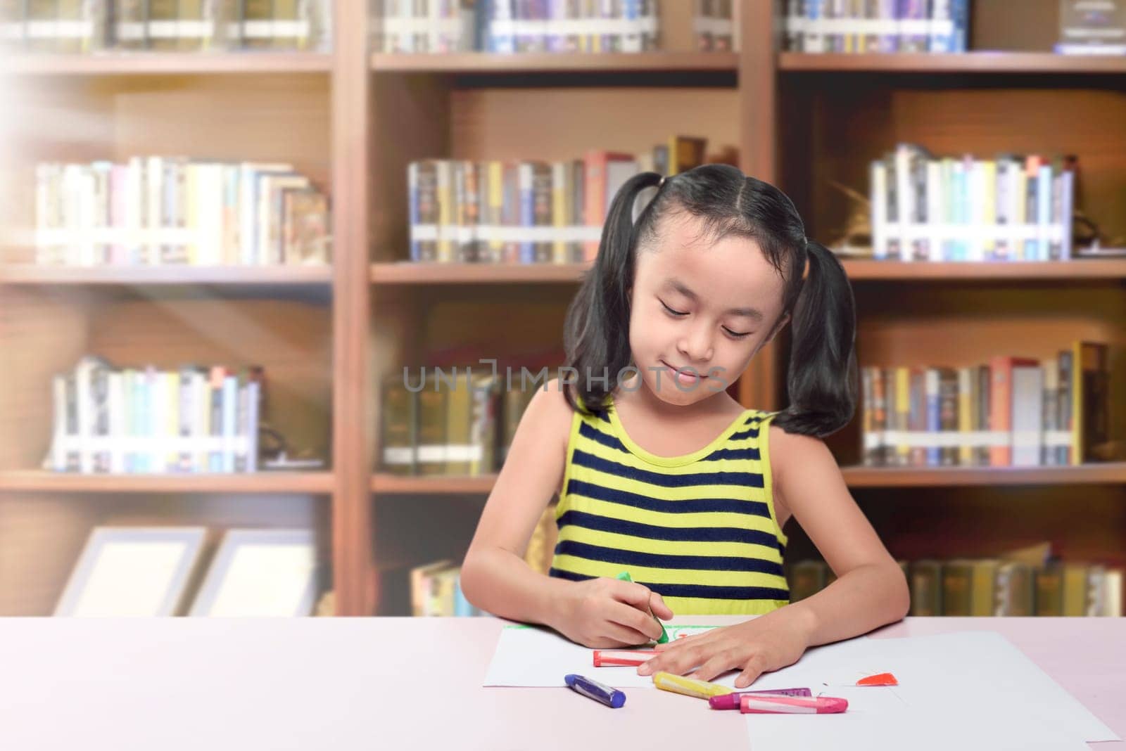 Happy asian little girl drawing on paper with crayon at table