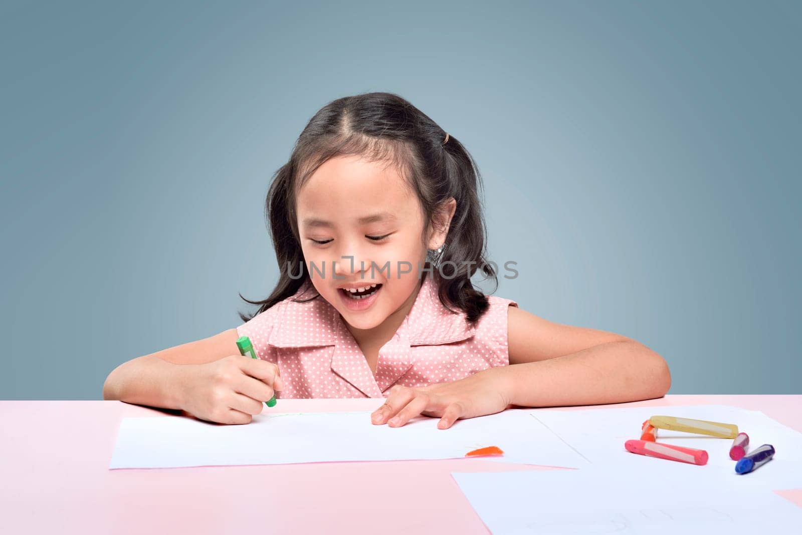 Beautiful asian little girl drawing with wax crayons over gray background