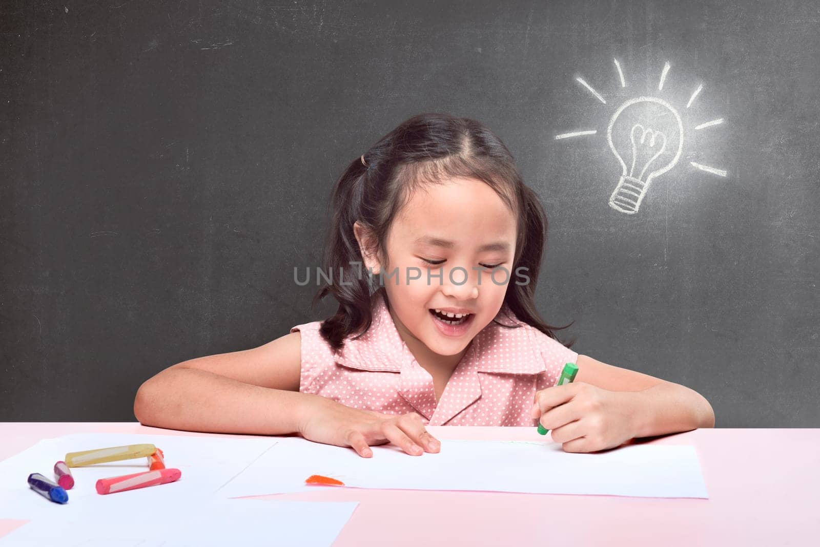 Cheerful asian little girl having new idea for drawing with crayon on black background