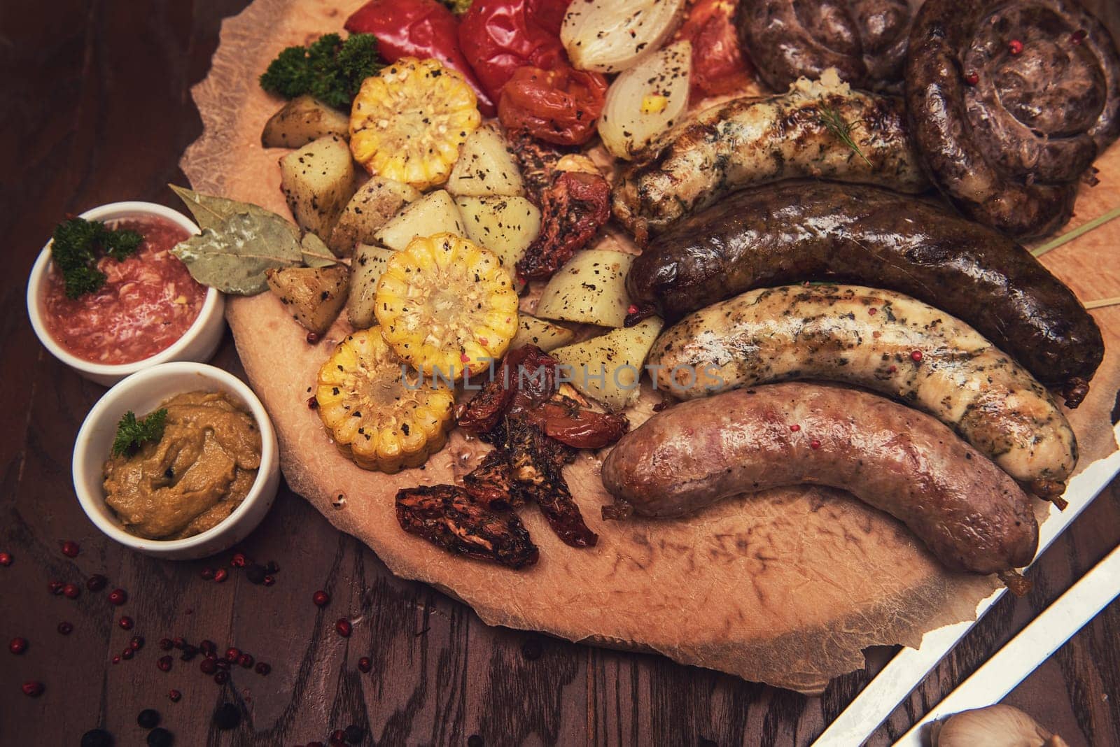 Grilled different meat and fish sausages with vegetables and spices on wooden background