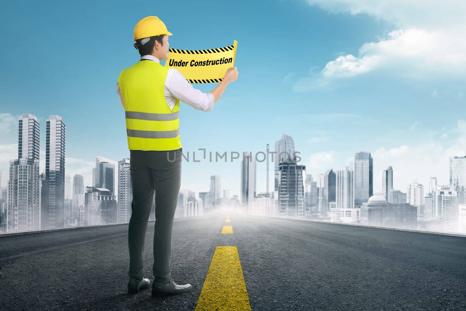 Back view of asian construction worker holding under construction signs in the road