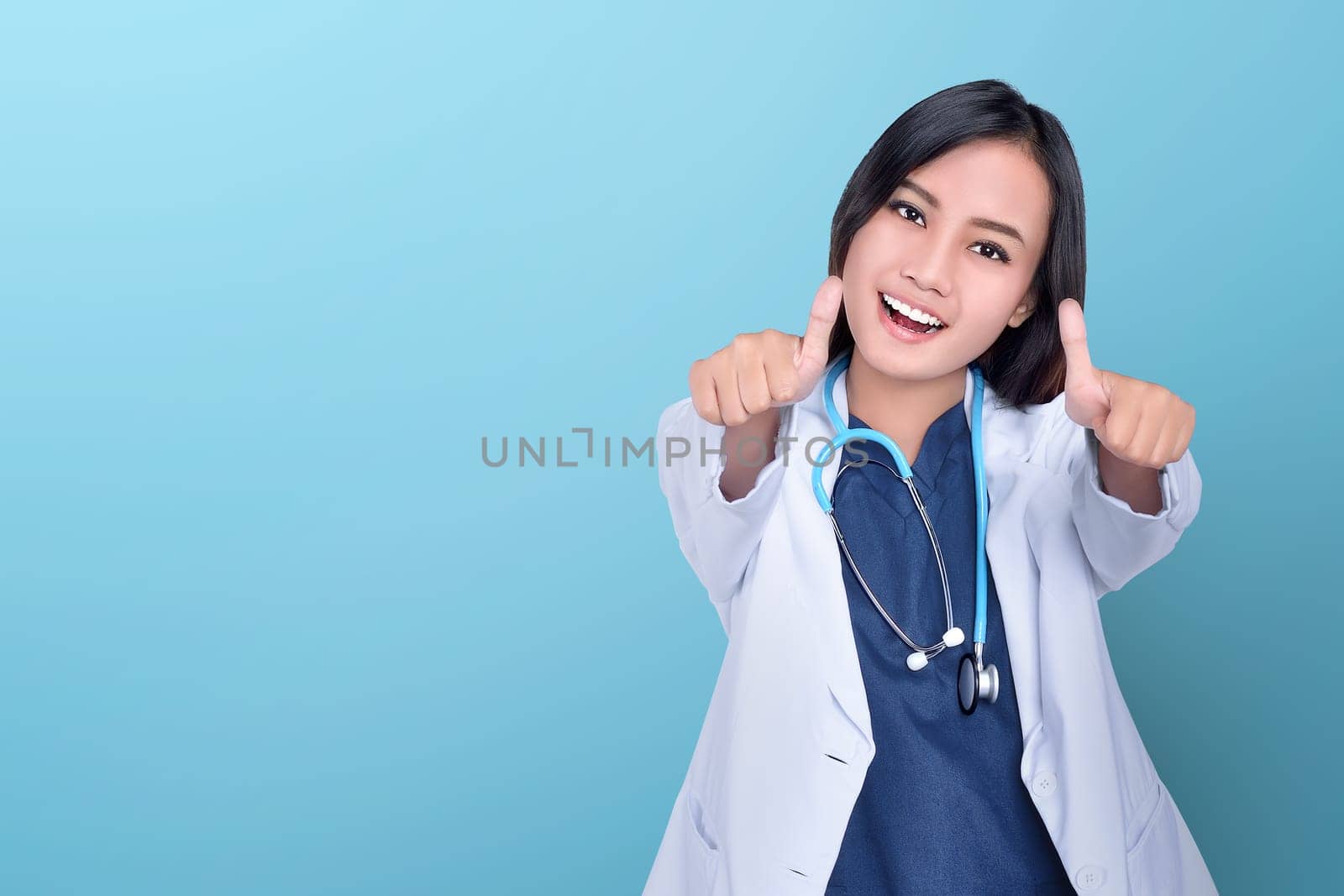 Happy asian woman doctor giving thumbs up over blue background