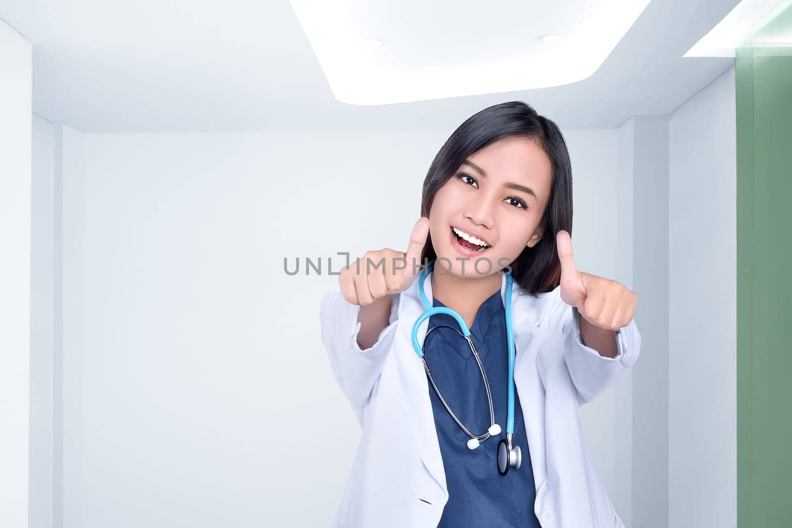 Beautiful asian female doctor in white coat showing thumbs up at clinic room