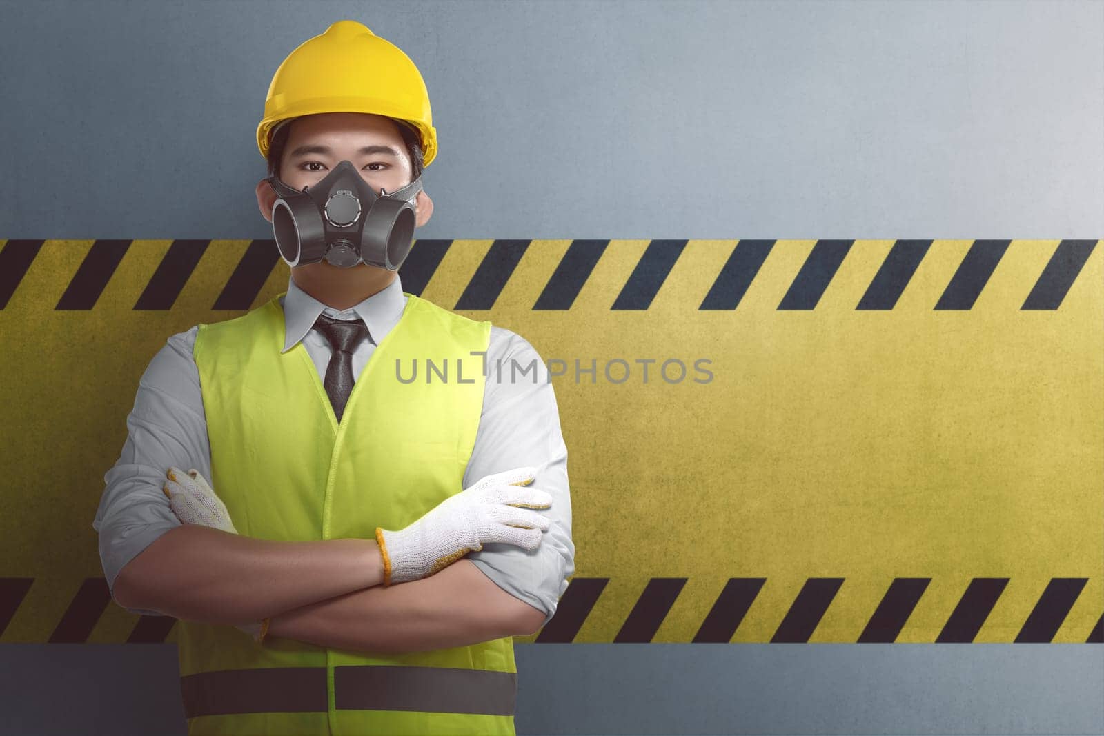 Young asian construction worker with crossed arm standing against yellow striped on the wall