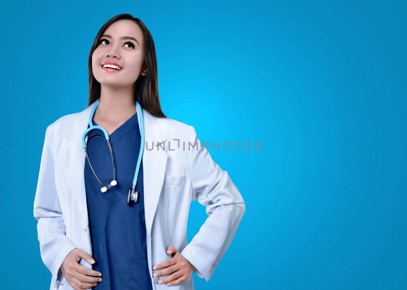 Young asian female doctor in white coat looking up with blue background