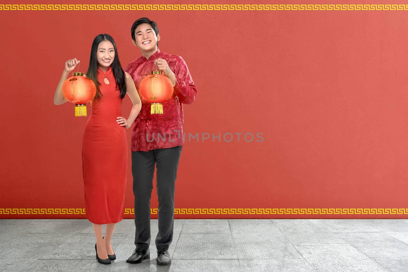 Young chinese couple with traditional dress holding red lanterns on red wall background. Happy Chinese New Year