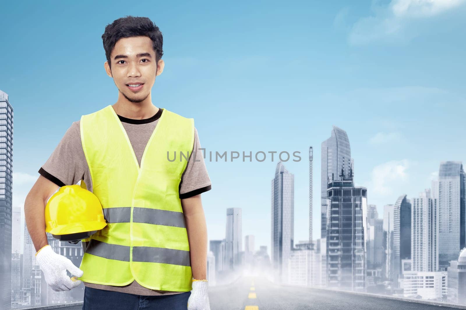 Attractive asian construction worker holding yellow helmet over cityscape background