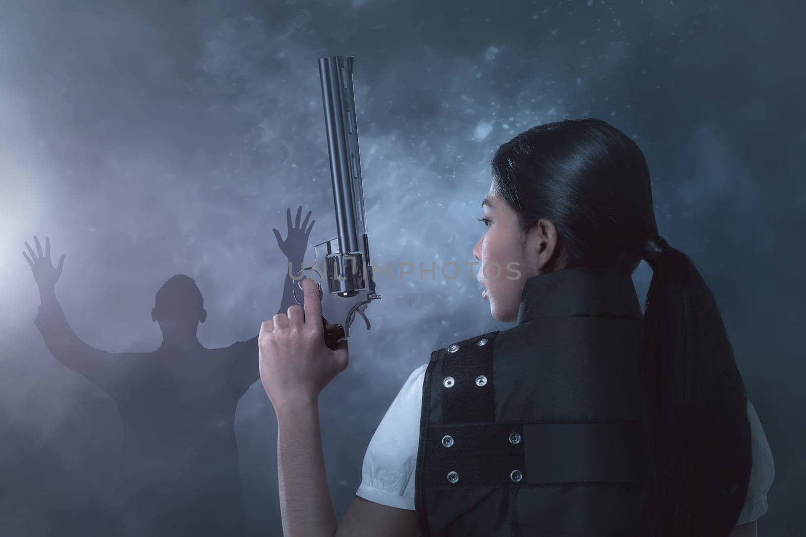 Young asian woman in a police uniform with pistol on her hands on dark background