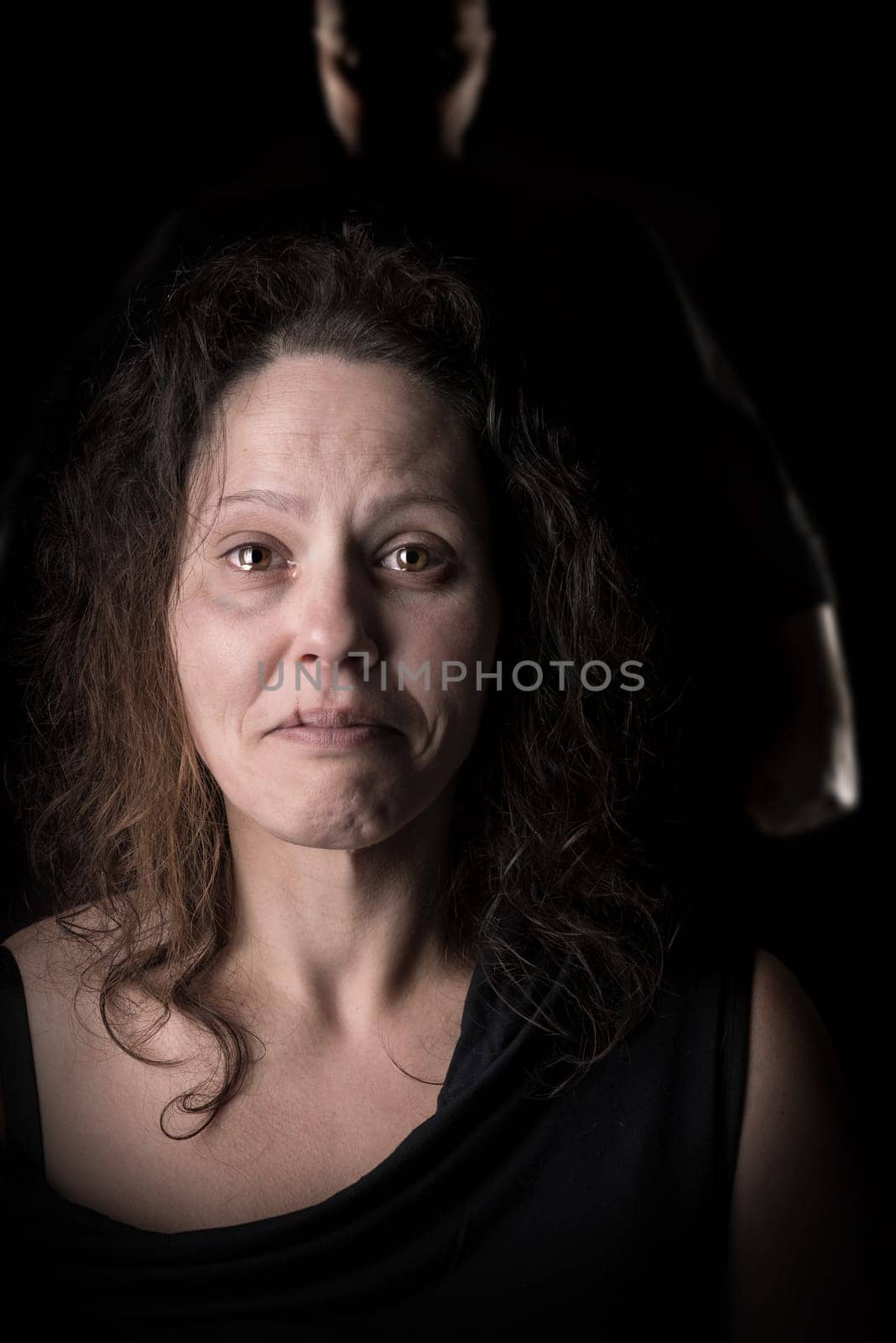 Abused woman victim of domestic violence, with husband silhouette in the background