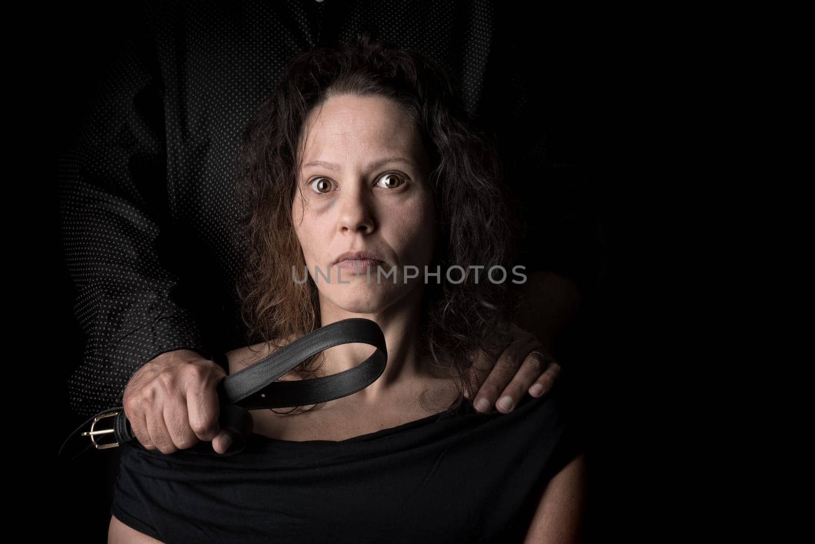 Abused woman victim of domestic violence, with husband hand holding a belt as a weapon.