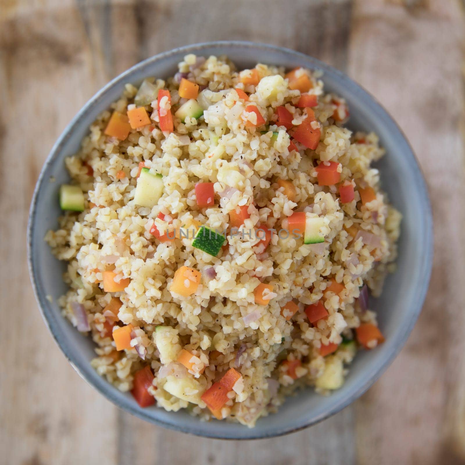 Bowl of vegan bulgur pilaf with carrots, red peppers, onions and zucchini.