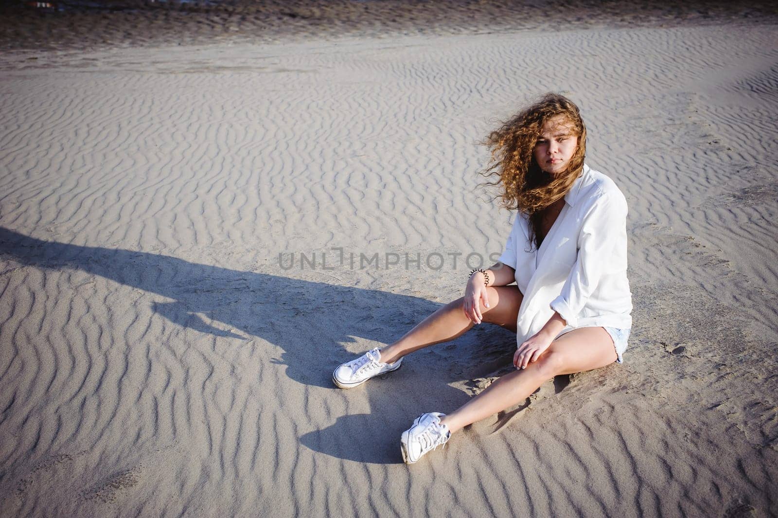 lovely young woman with curly hair, the romance of youth, a journey walk on a warm summer sunny day on a sandy beach with water