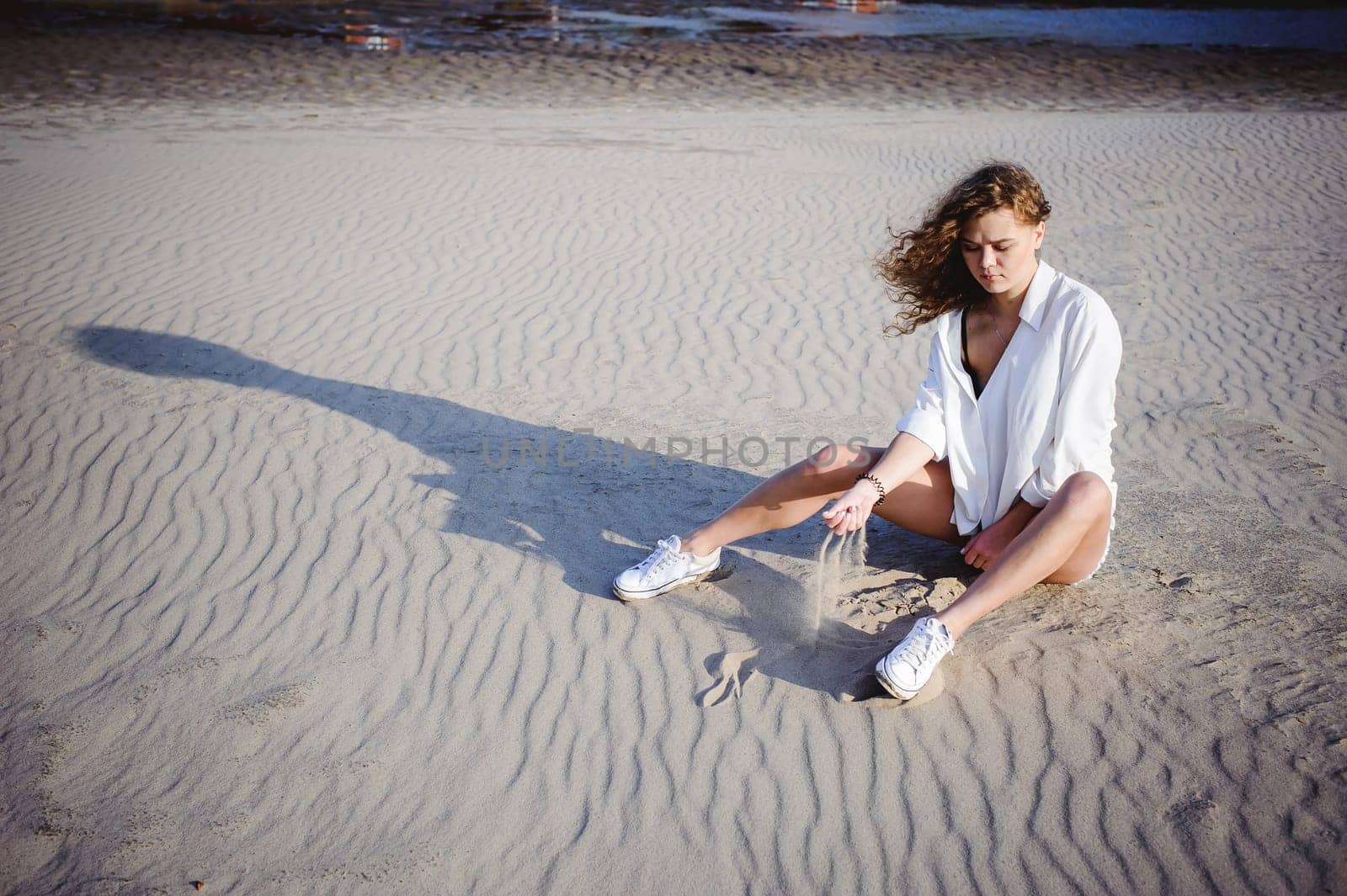 lovely young woman with curly hair, the romance of youth, a journey walk on a warm summer sunny day on a sandy beach with water