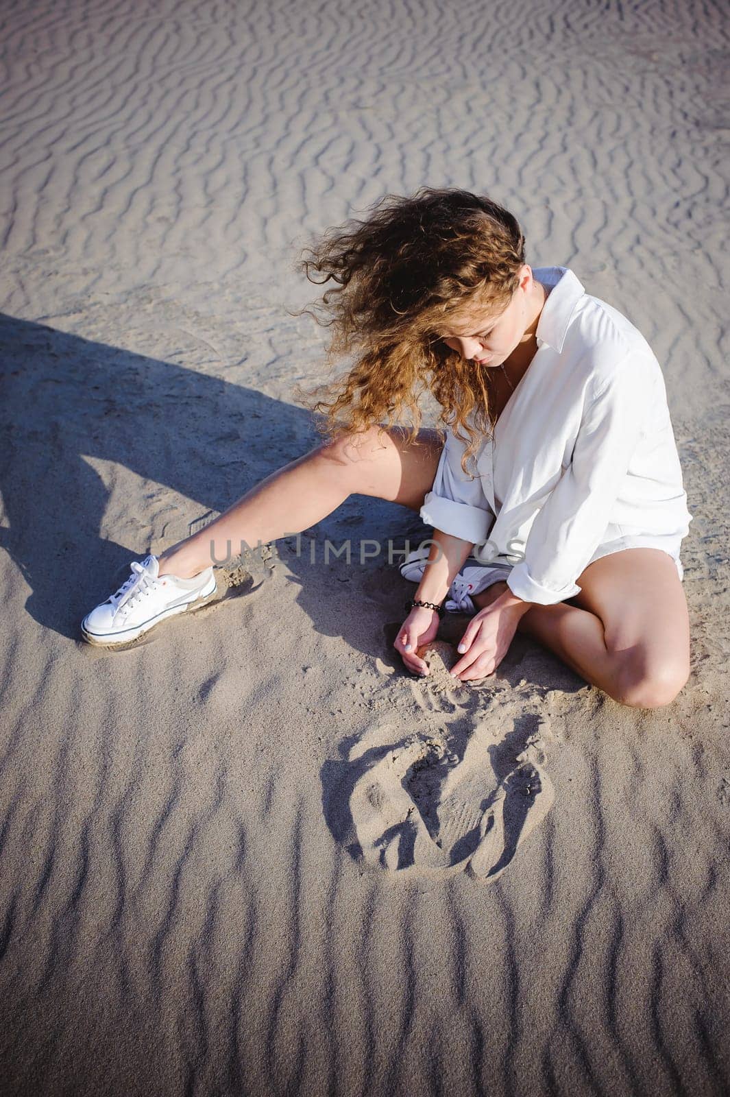 lovely young woman with curly hair, the romance of youth, a journey walk on a warm summer sunny day on a sandy beach with water