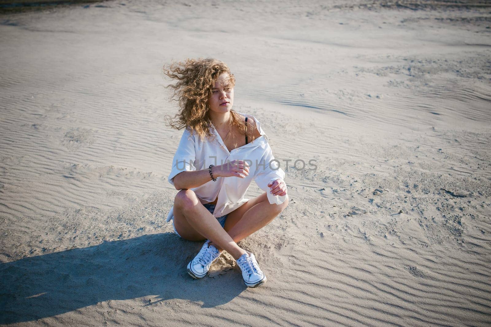 lovely young woman with curly hair, the romance of youth, a journey walk on a warm summer sunny day on a sandy beach with water