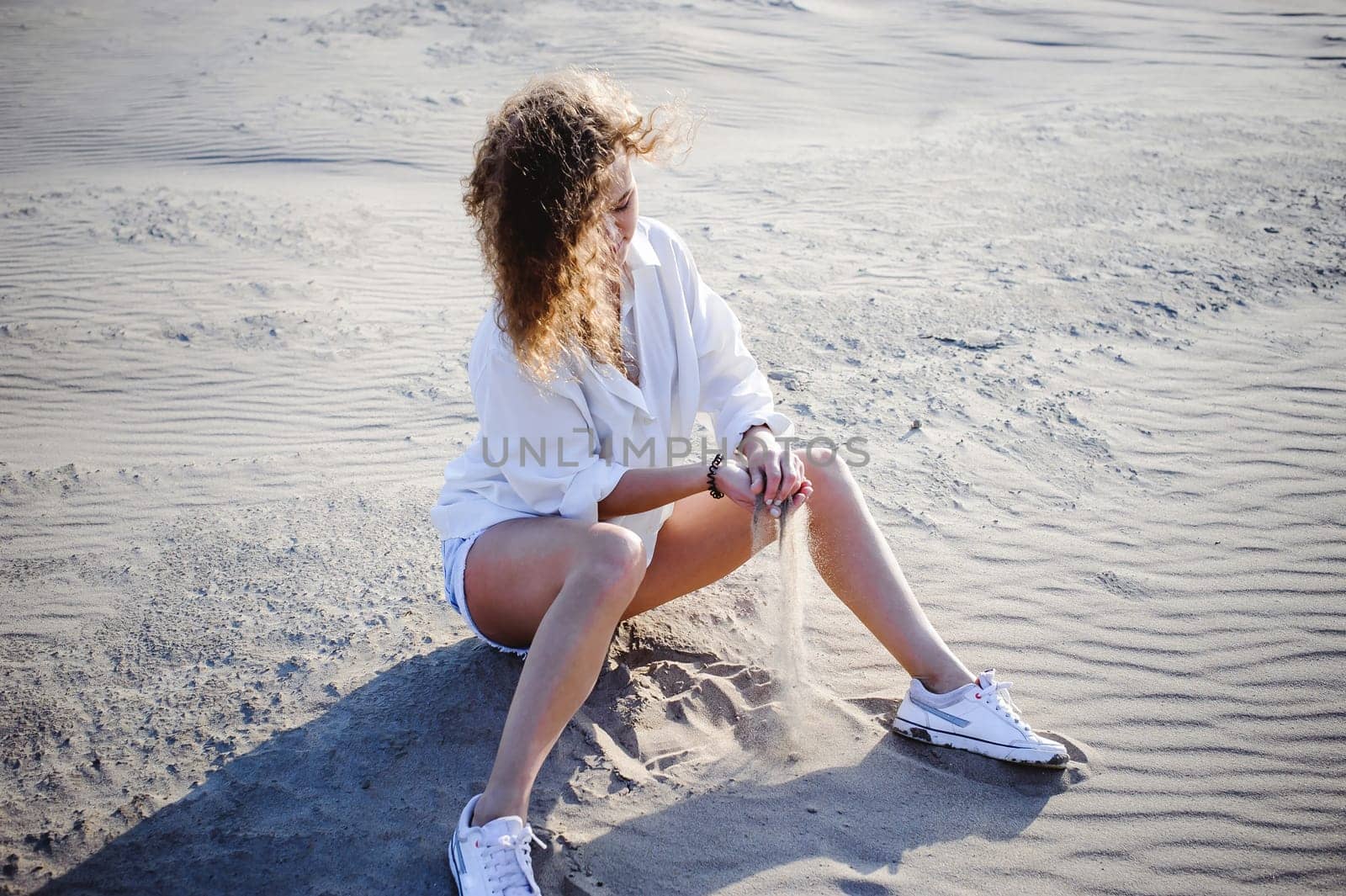 lovely young woman with curly hair, the romance of youth, a journey walk on a warm summer sunny day on a sandy beach with water