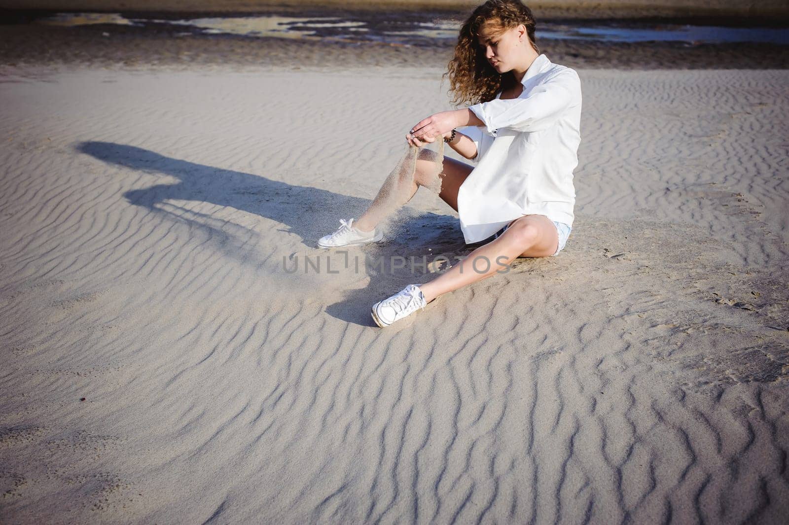 lovely young woman with curly hair, the romance of youth, a journey walk on a warm summer sunny day on a sandy beach with water