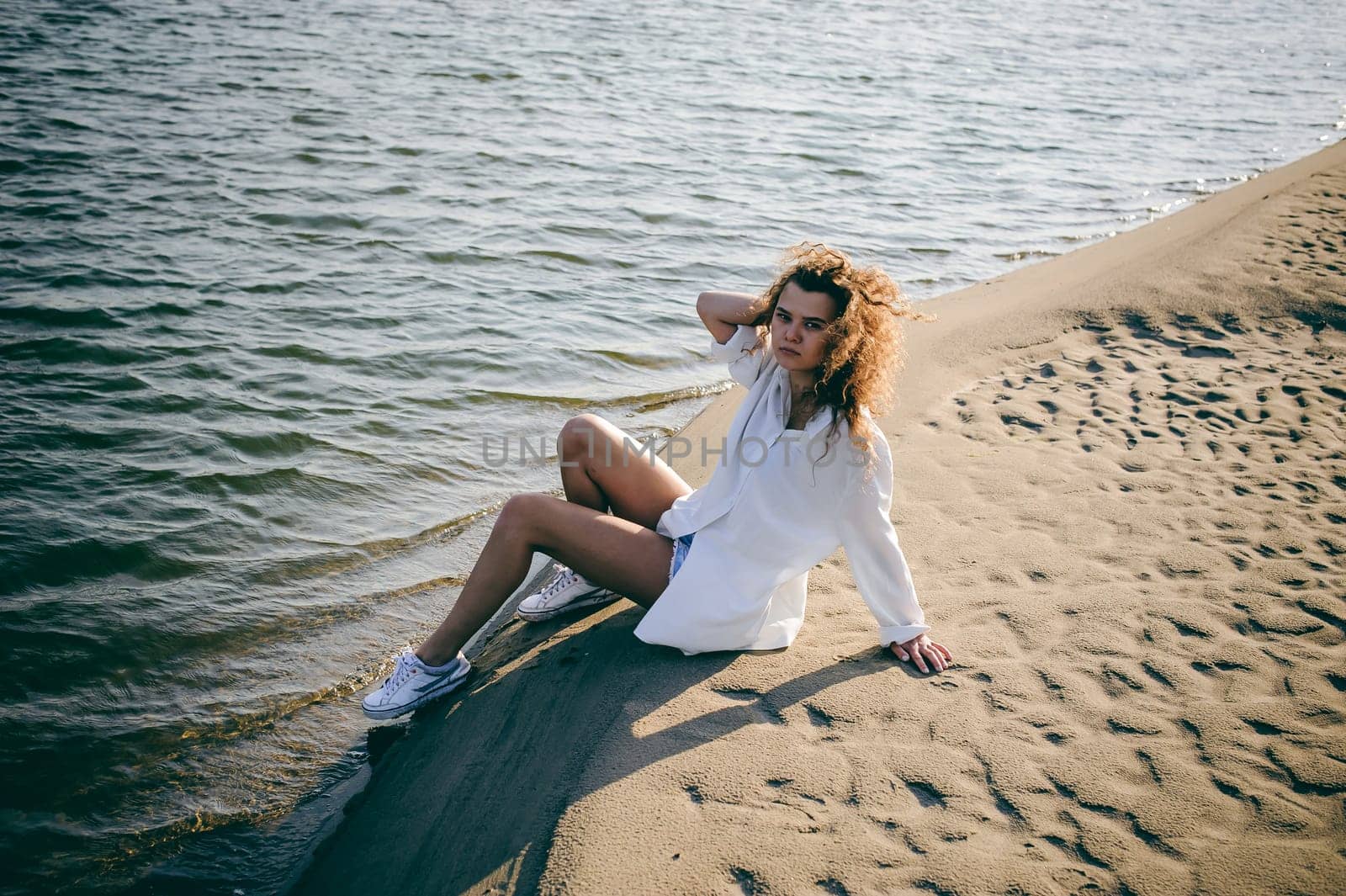 lovely young woman with curly hair, the romance of youth, a journey walk on a warm summer sunny day on a sandy beach with water