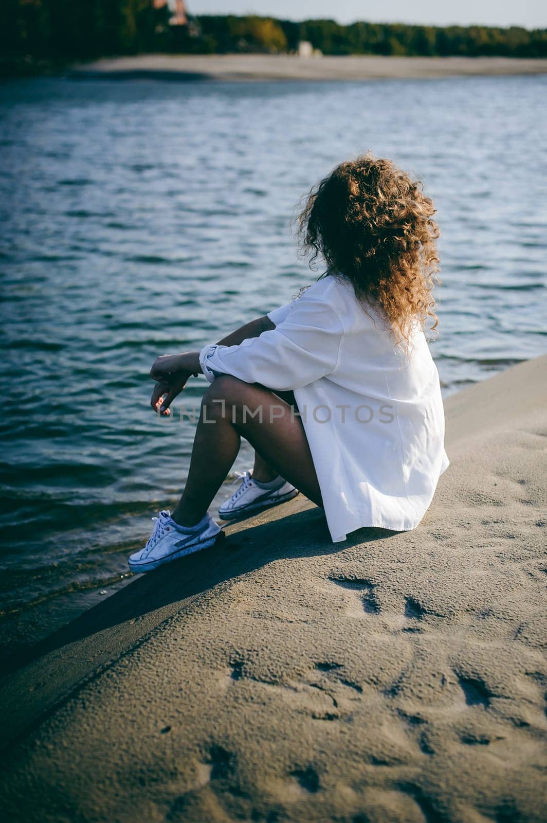 lovely young woman with curly hair, the romance of youth, a journey walk on a warm summer sunny day on a sandy beach with water