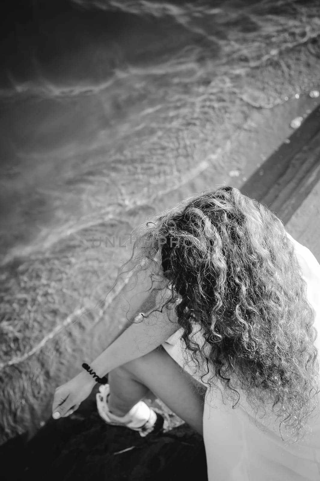 lovely young woman with curly hair, the romance of youth, a journey walk on a warm summer sunny day on a sandy beach with water
