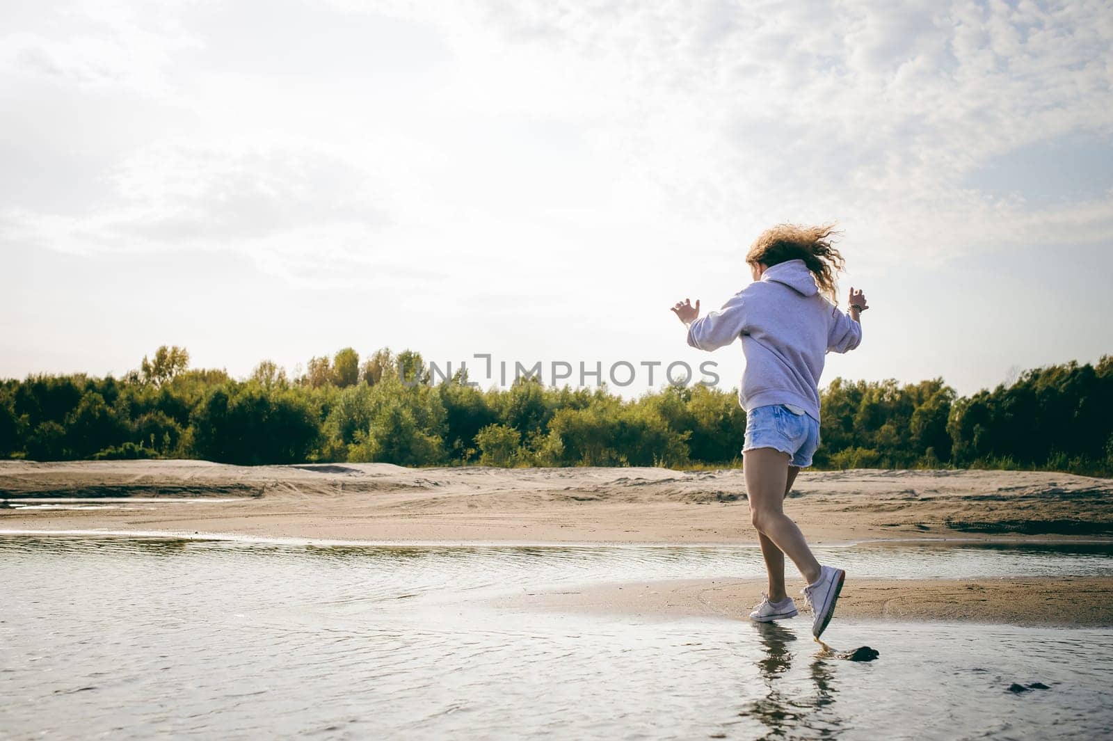 lovely young woman with curly hair, the romance of youth, a journey walk on a warm summer sunny day on a sandy beach with water