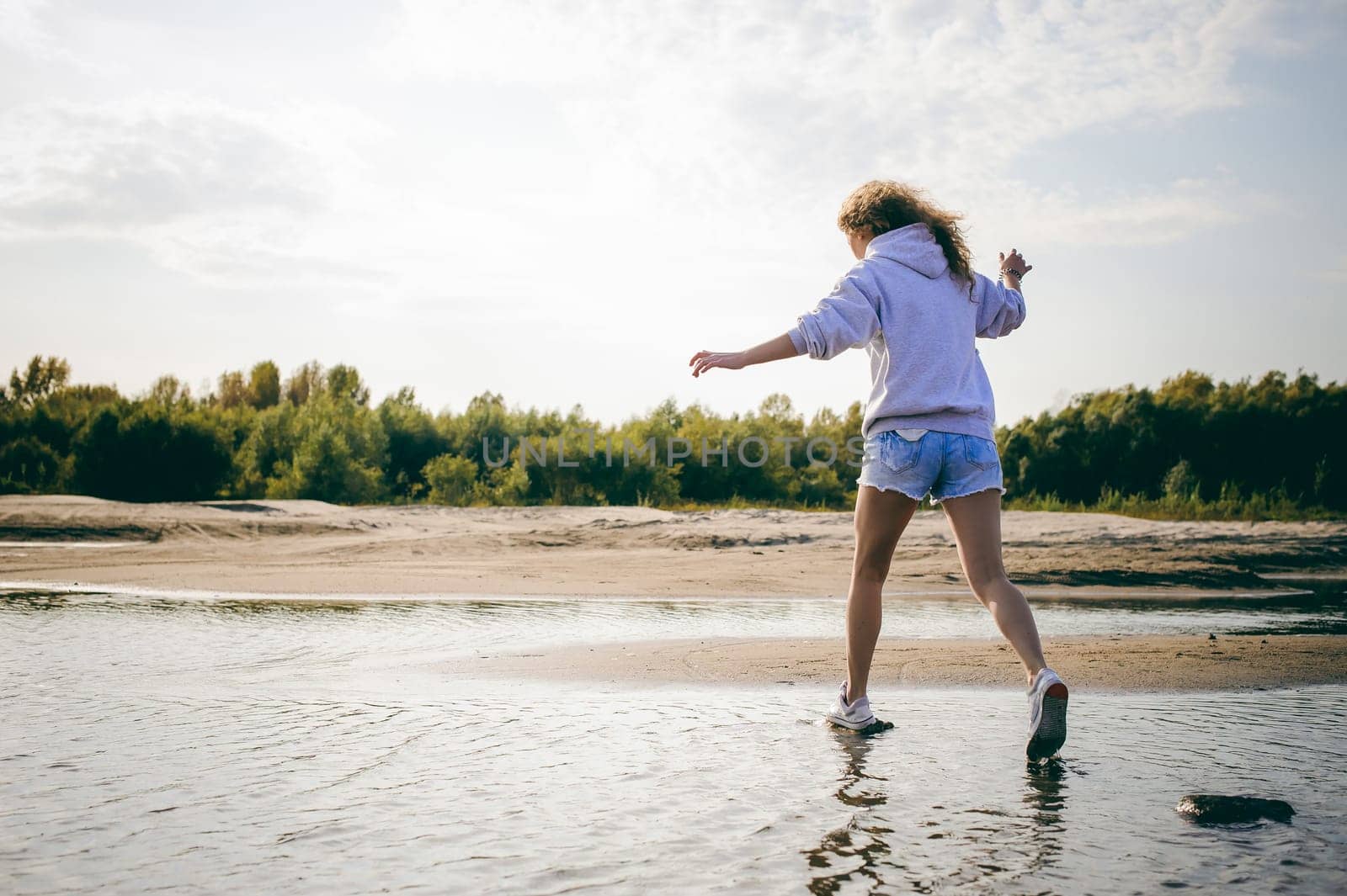 lovely young woman with curly hair, the romance of youth, a journey walk on a warm summer sunny day on a sandy beach with water