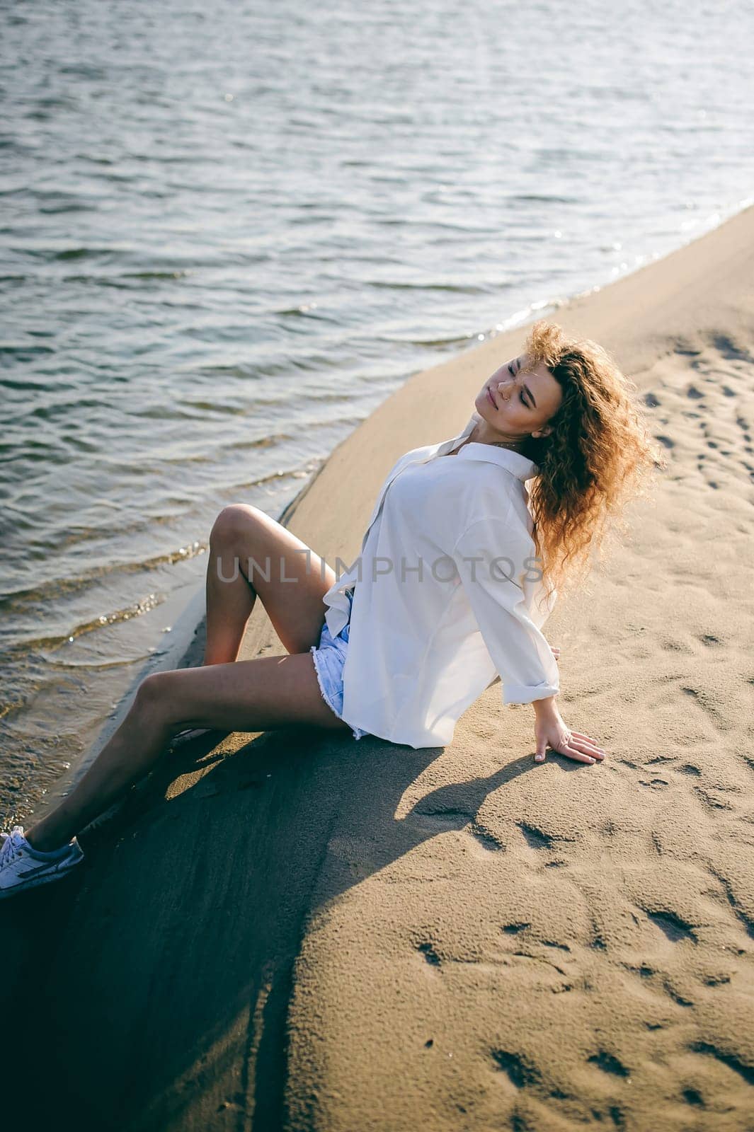 lovely young woman with curly hair, the romance of youth, a journey walk on a warm summer sunny day on a sandy beach with water