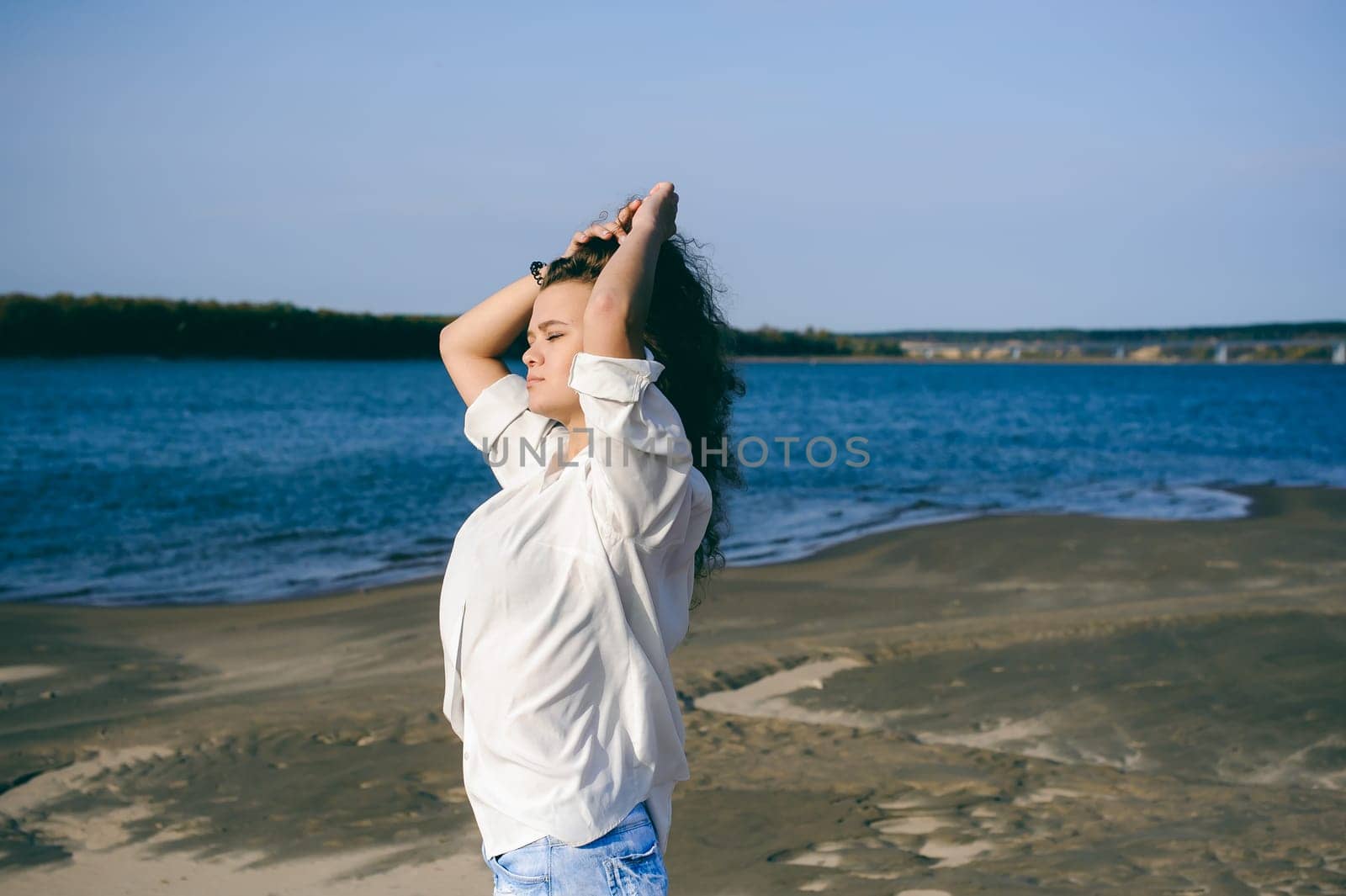 lovely young woman with curly hair, the romance of youth, a journey walk on a warm summer sunny day on a sandy beach with water