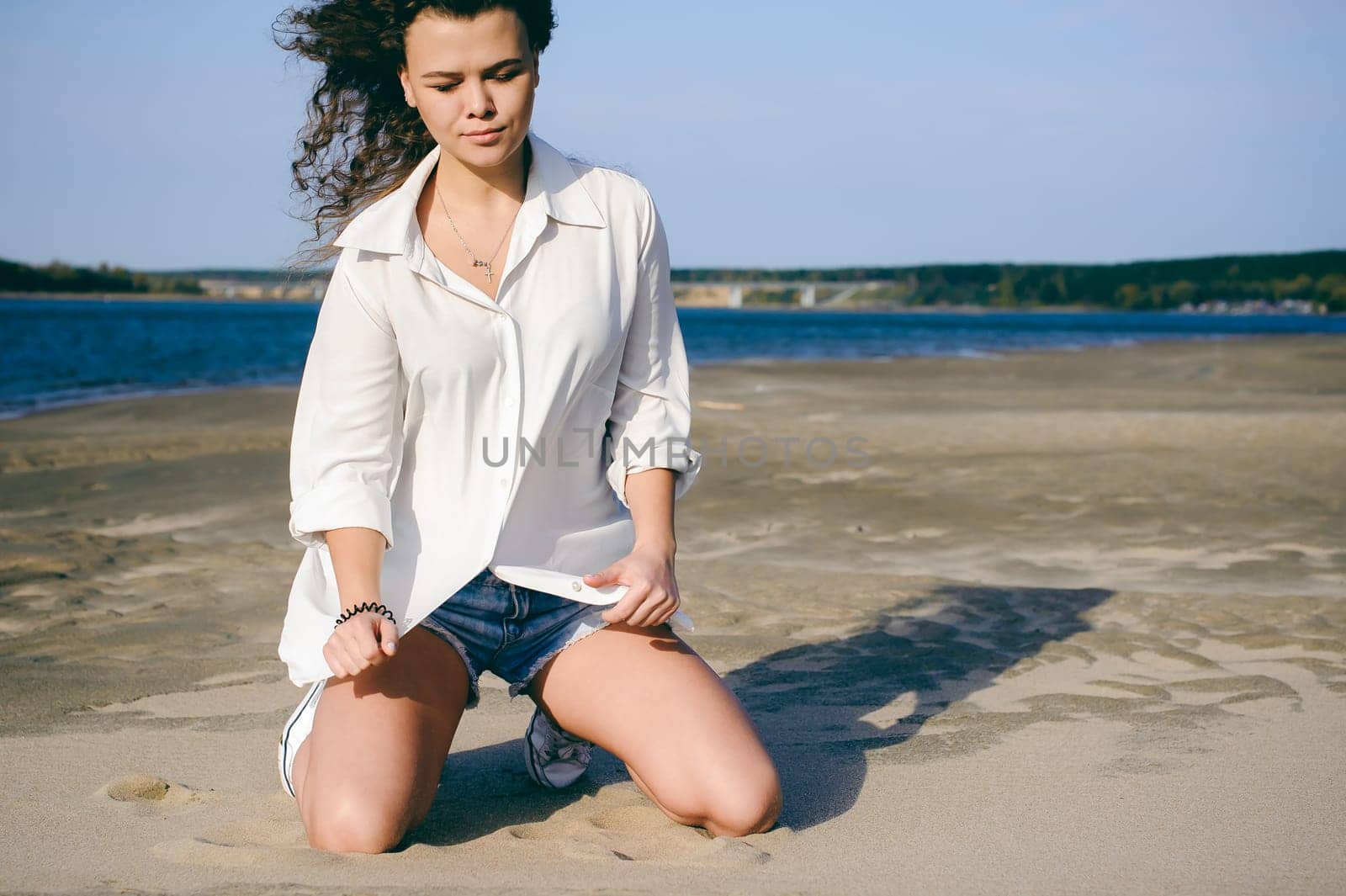 lovely young woman with curly hair, the romance of youth, a journey walk on a warm summer sunny day on a sandy beach with water