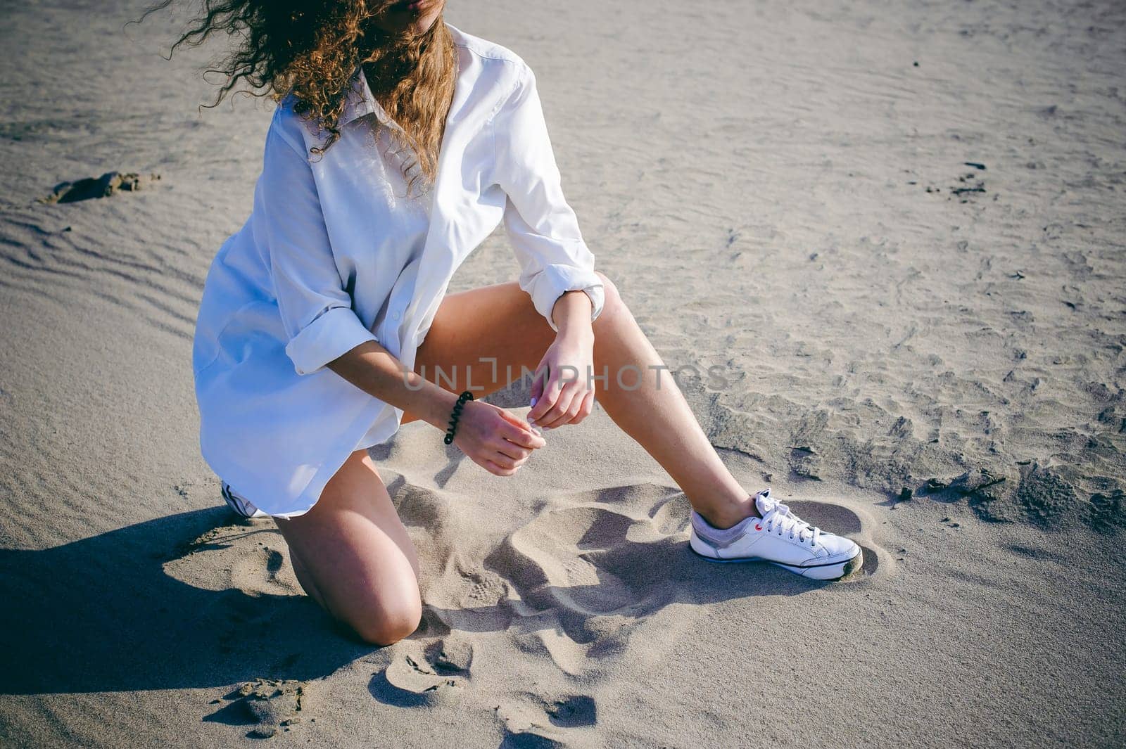 lovely young woman with curly hair, the romance of youth, a journey walk on a warm summer sunny day on a sandy beach with water