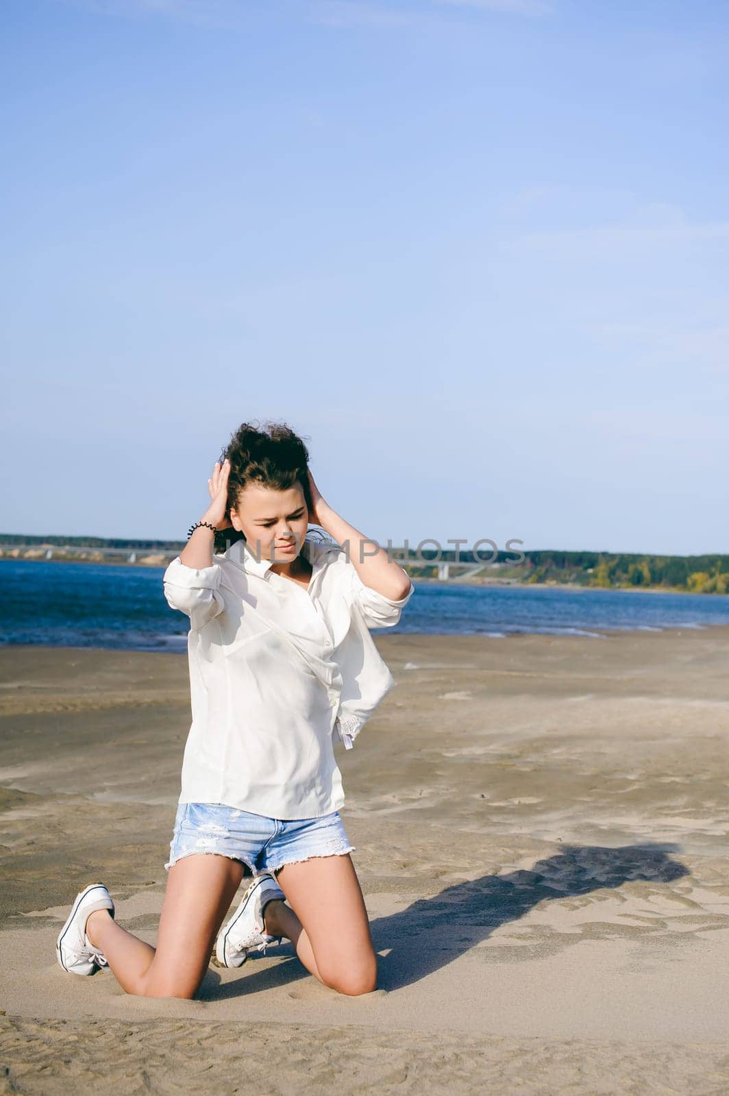 lovely young woman with curly hair, the romance of youth, a journey walk on a warm summer sunny day on a sandy beach with water