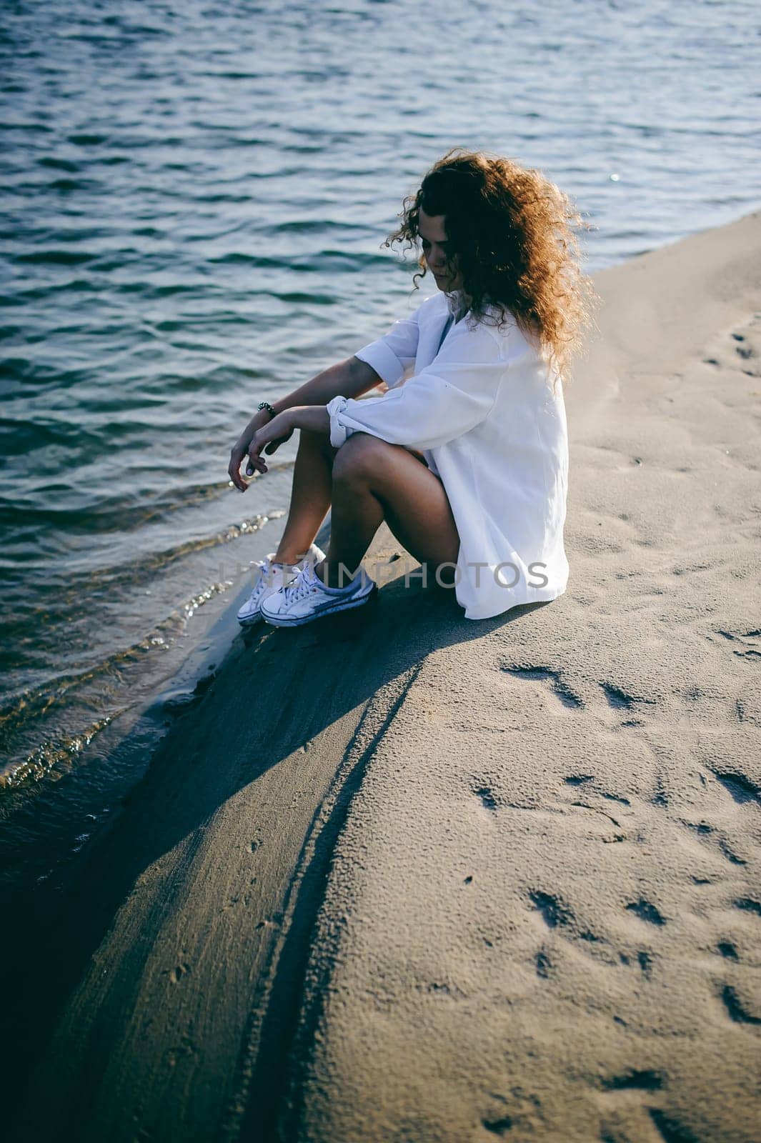 lovely young woman with curly hair, the romance of youth, a journey walk on a warm summer sunny day on a sandy beach with water