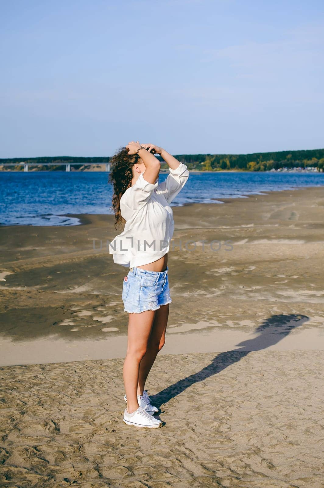 lovely young woman with curly hair, the romance of youth, a journey walk on a warm summer sunny day on a sandy beach with water