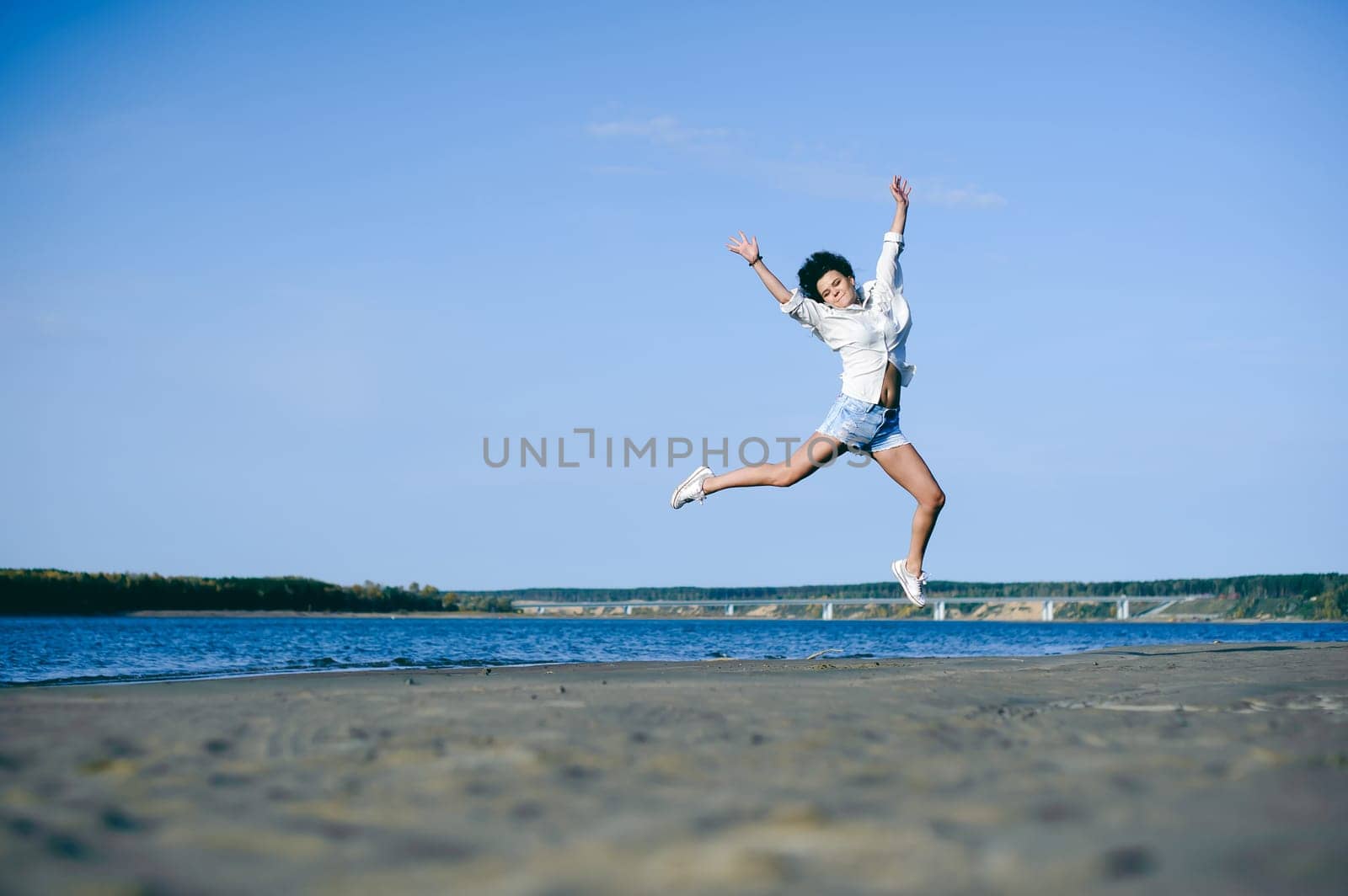lovely young woman with curly hair, the romance of youth, a journey walk on a warm summer sunny day on a sandy beach with water