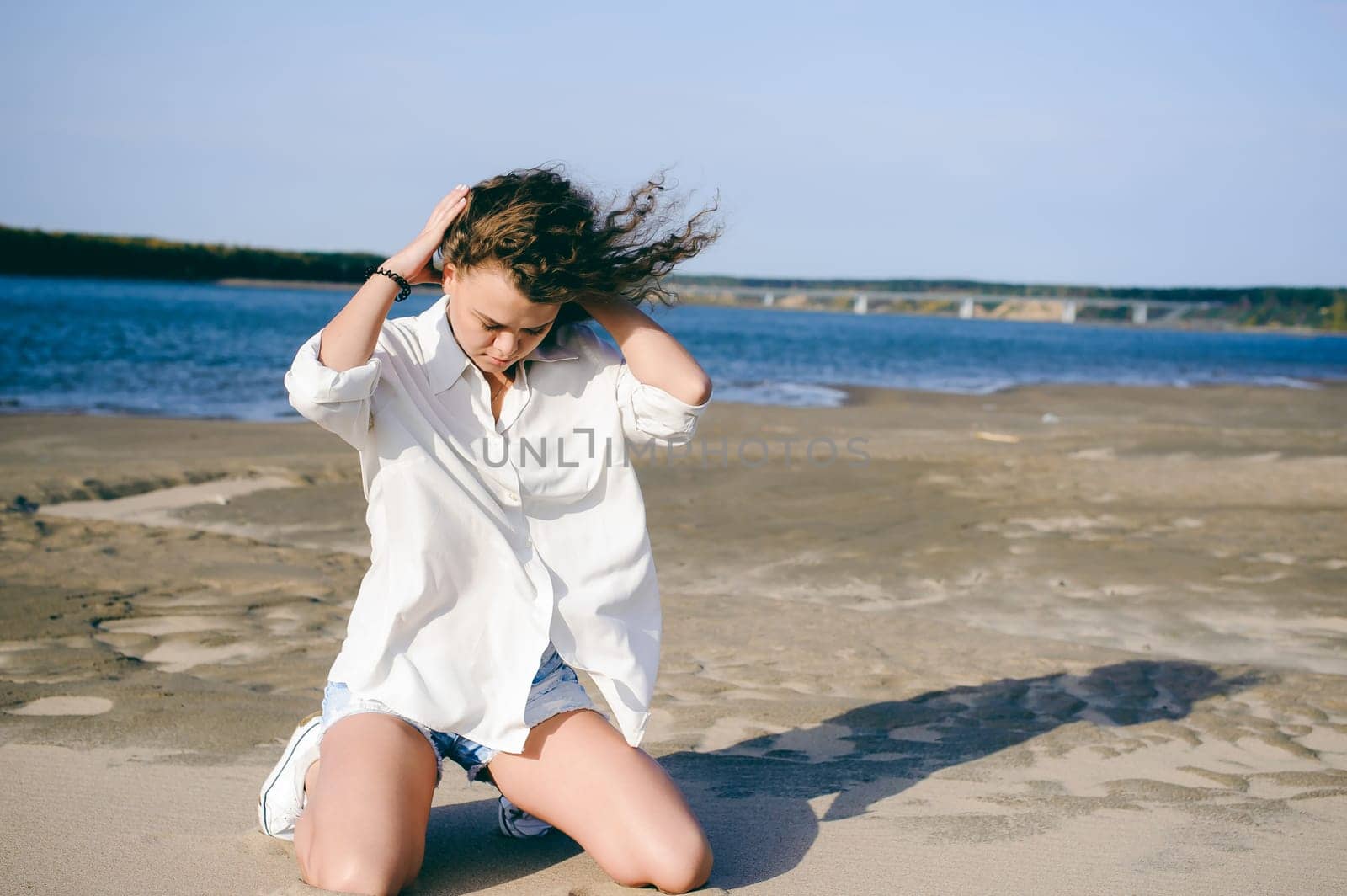 lovely young woman with curly hair, the romance of youth, a journey walk on a warm summer sunny day on a sandy beach with water
