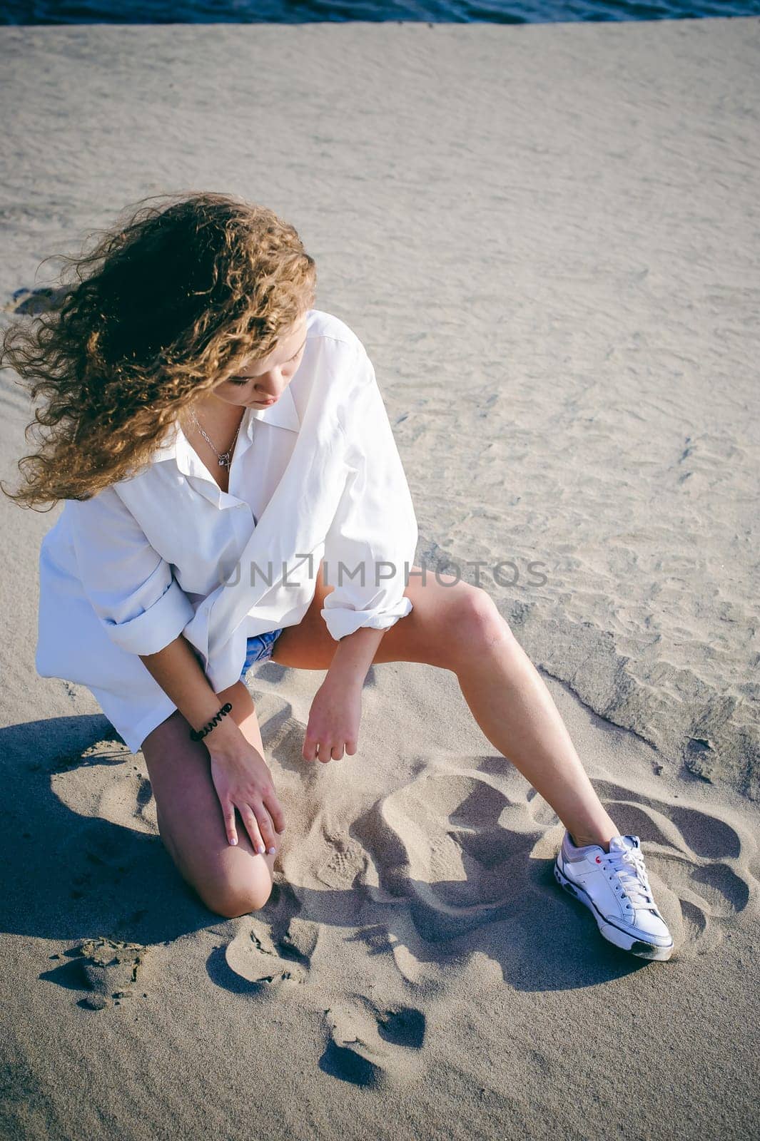 lovely young woman with curly hair, the romance of youth, a journey walk on a warm summer sunny day on a sandy beach with water