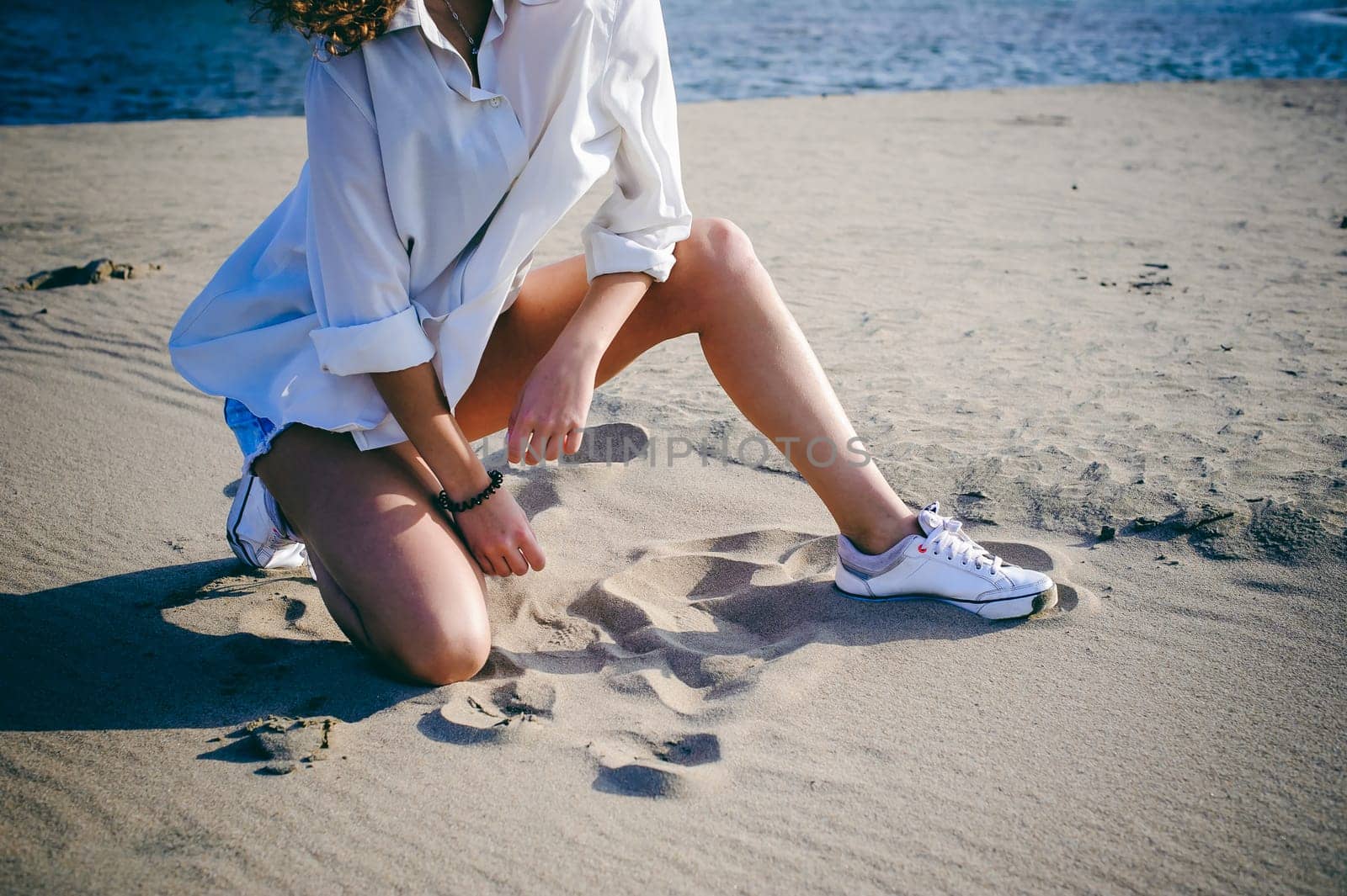 lovely young woman with curly hair, the romance of youth, a journey walk on a warm summer sunny day on a sandy beach with water