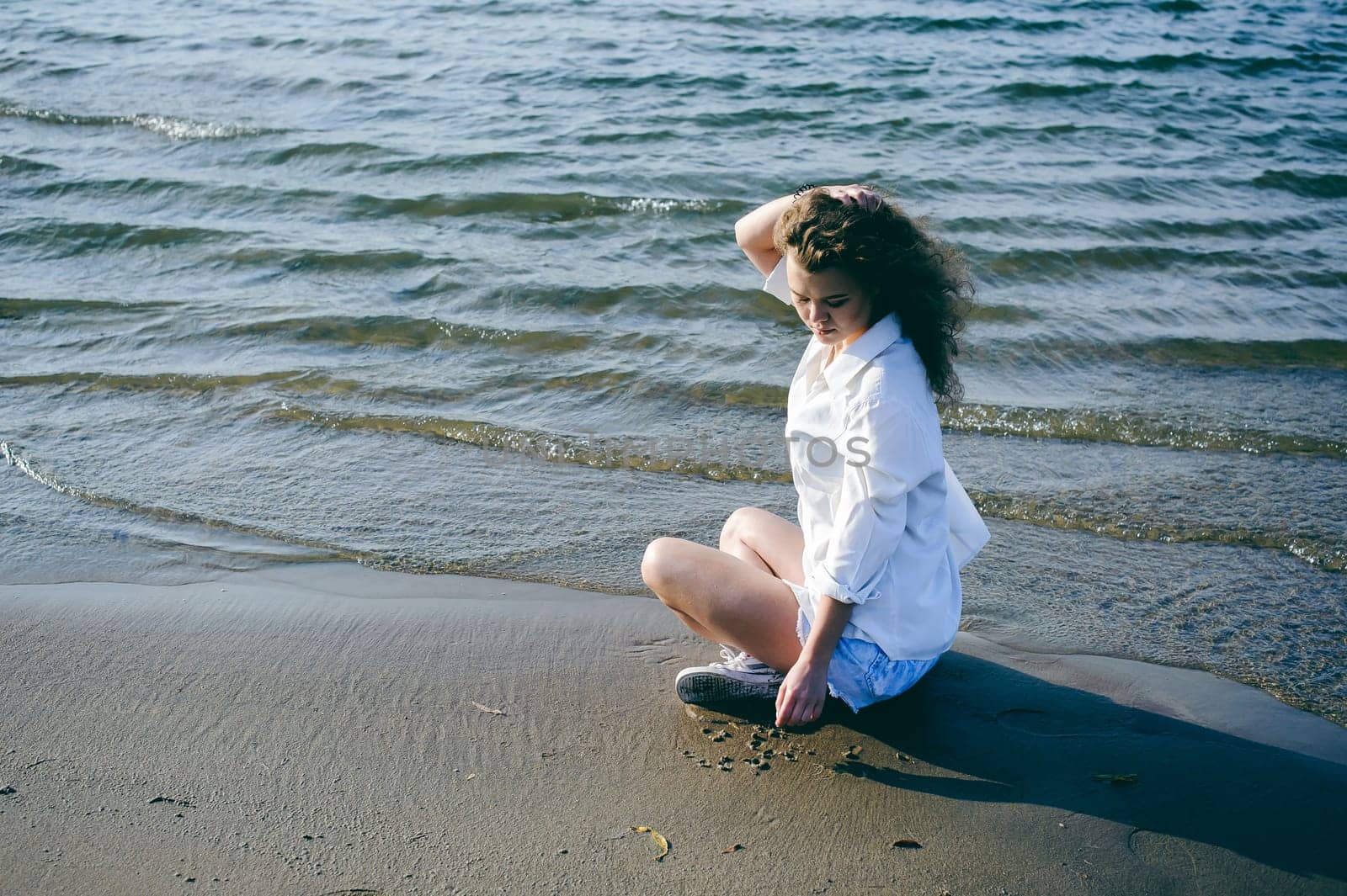lovely young woman with curly hair, the romance of youth, a journey walk on a warm summer sunny day on a sandy beach with water