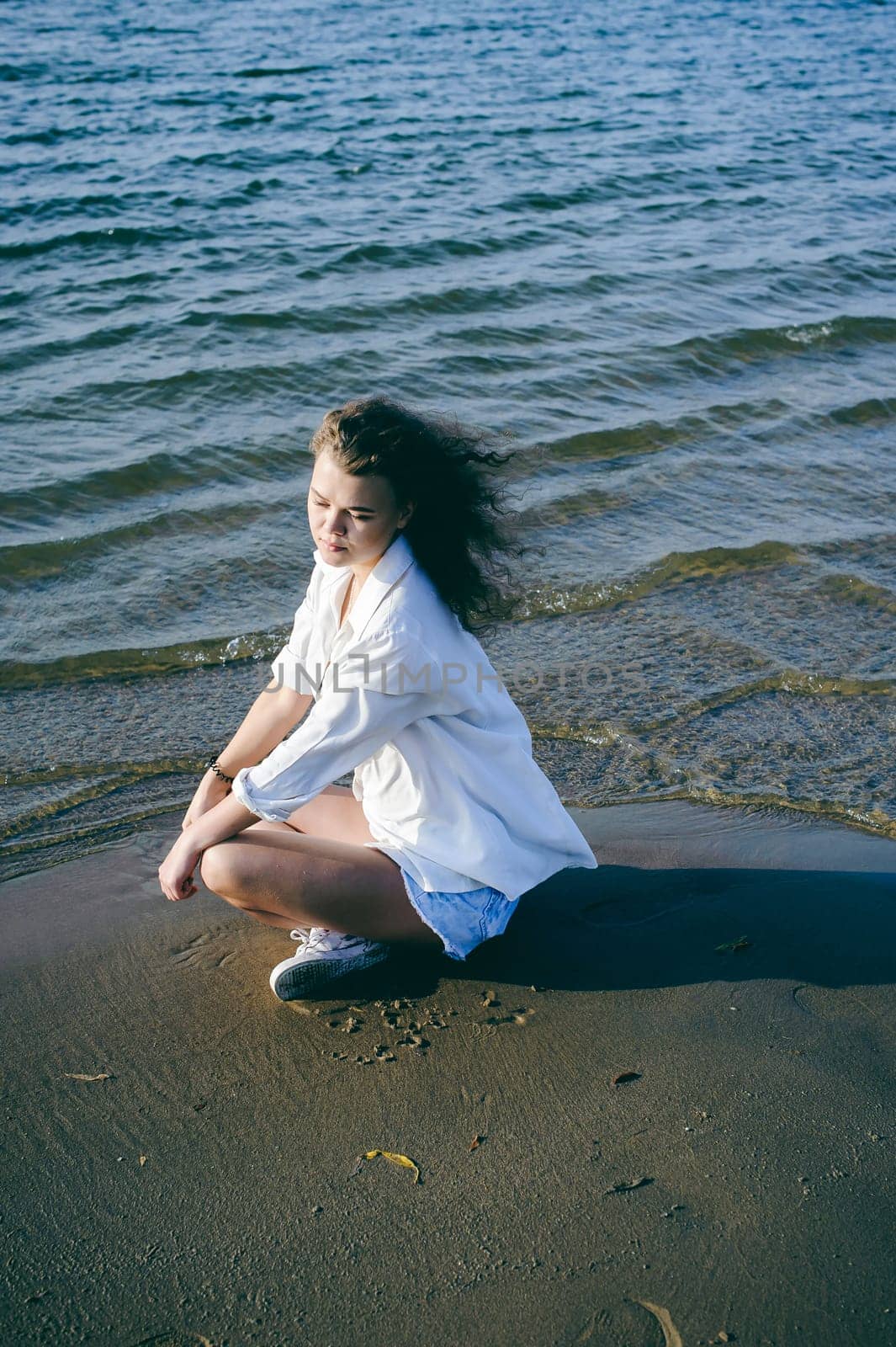 lovely young woman with curly hair, the romance of youth, a journey walk on a warm summer sunny day on a sandy beach with water