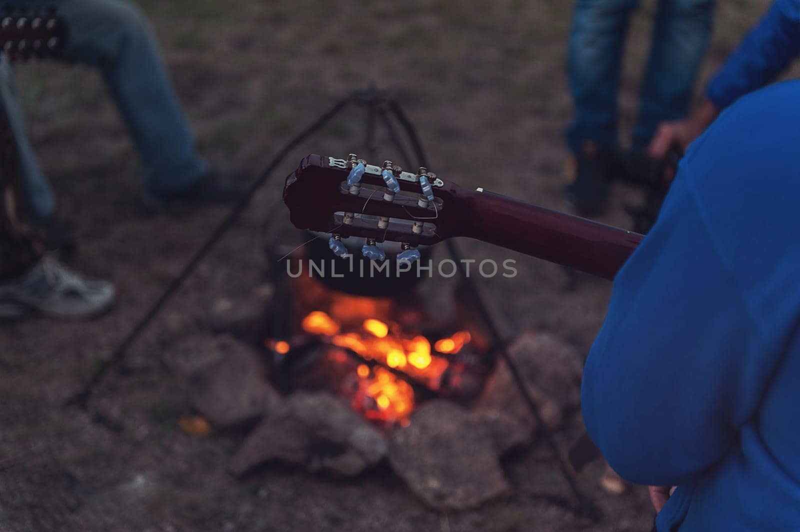 Closeup photo of the man playing o guitar near the campfire