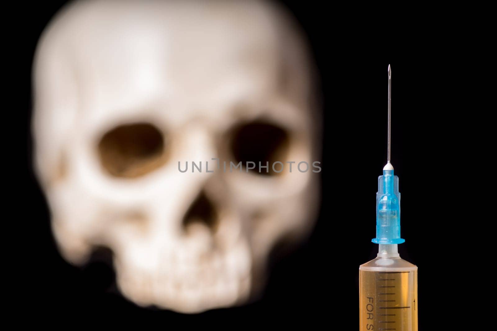 Syringe with brown liquid and blurry skull isolated on black background